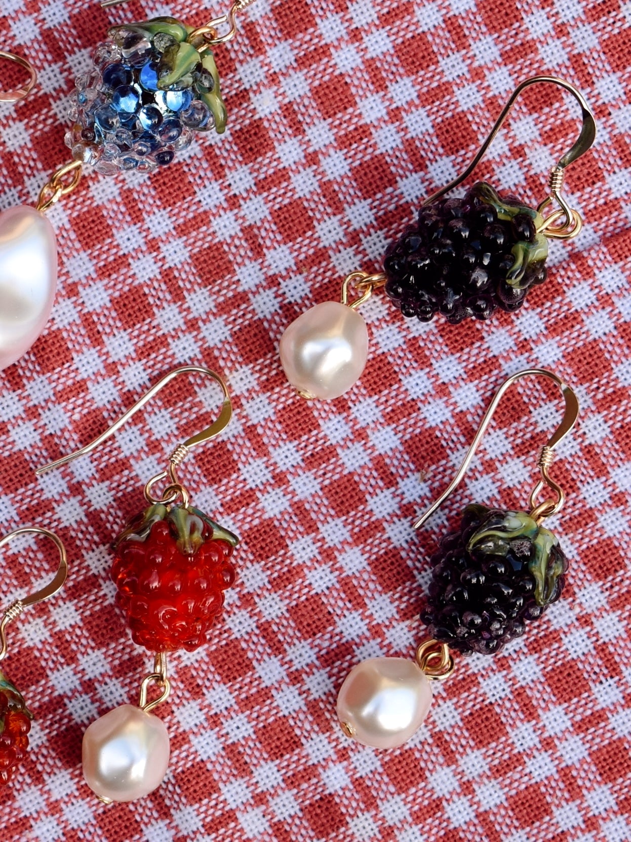 Earrings with berry and pearl designs on a red and white checkered background