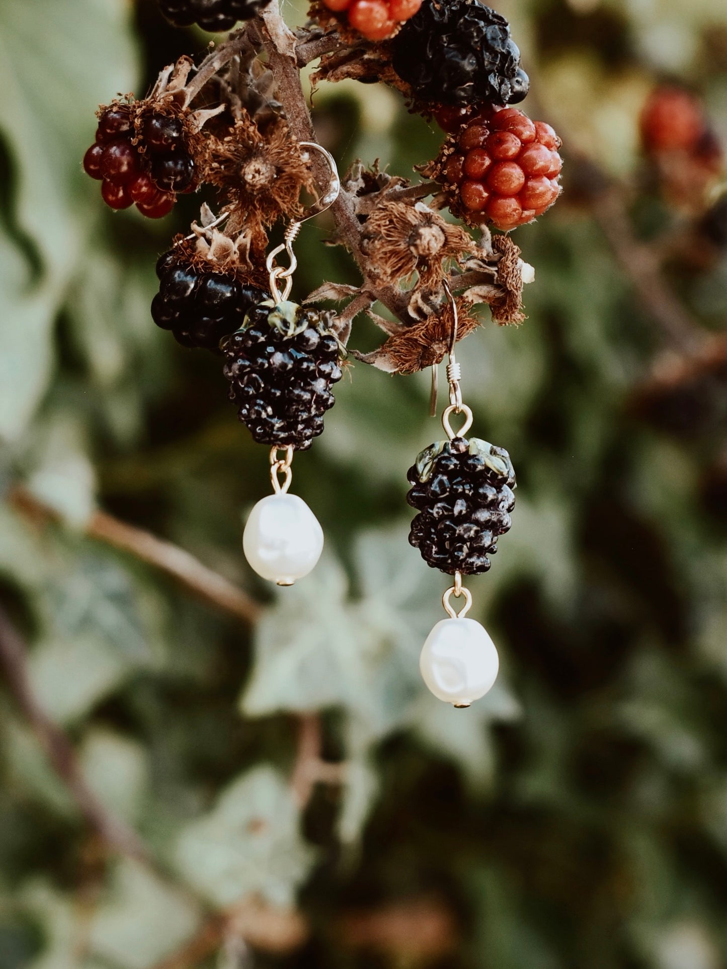 Earrings with black and white beads hanging from a branch with berries.
