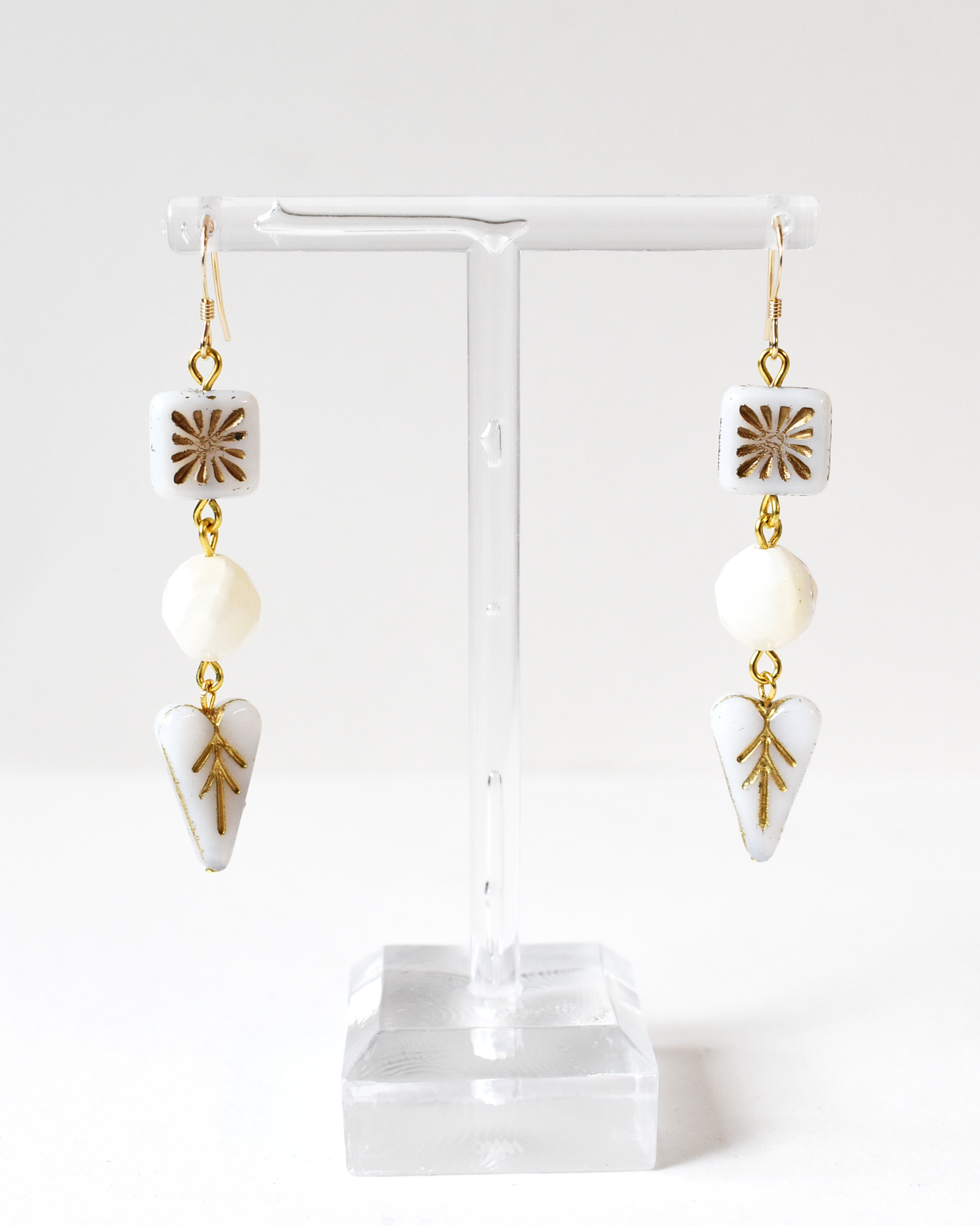 Pair of earrings with gold accents and white stones on a clear stand against a white background