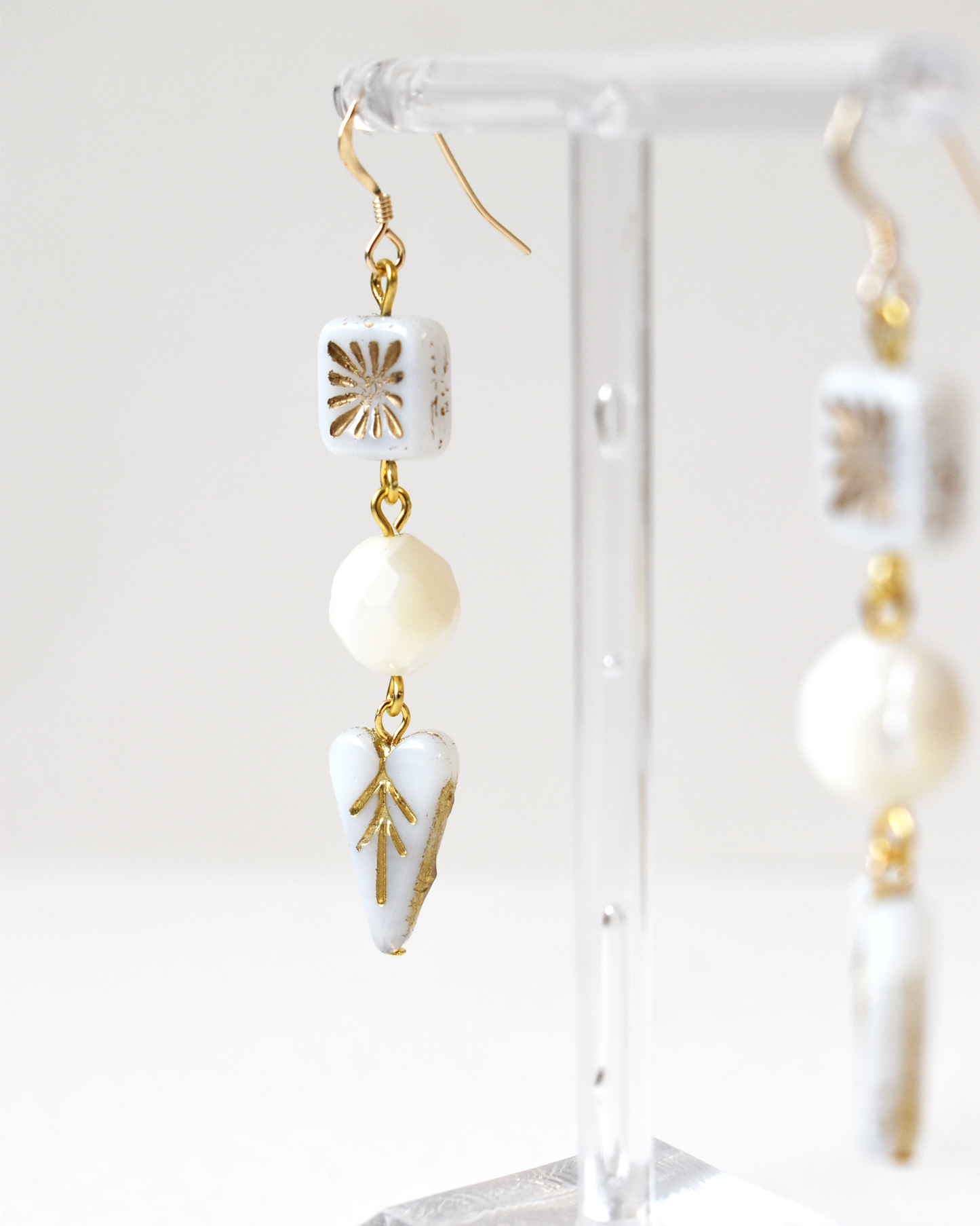 White and gold earrings on a clear stand against a white background