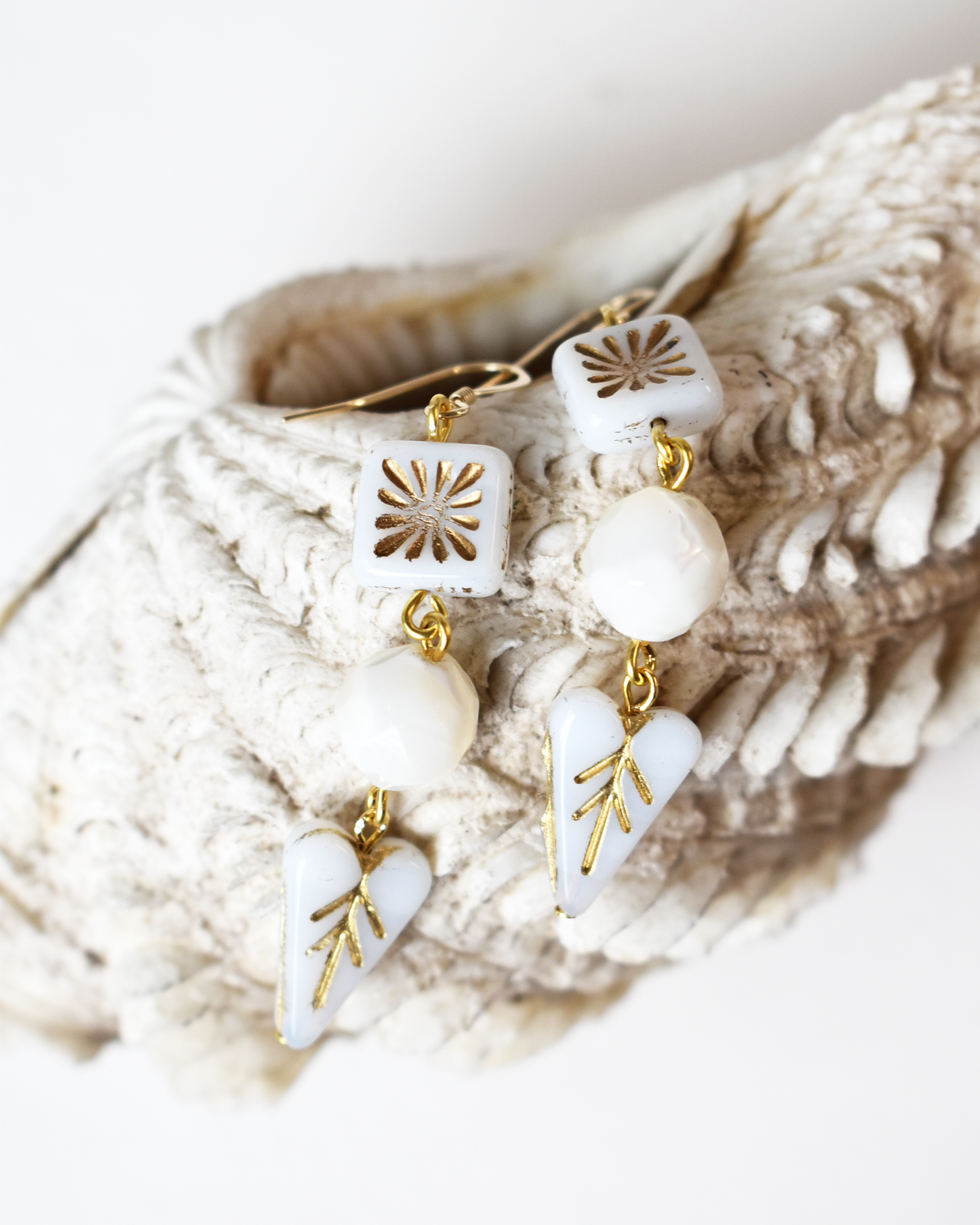 White and gold earrings on a textured beige surface