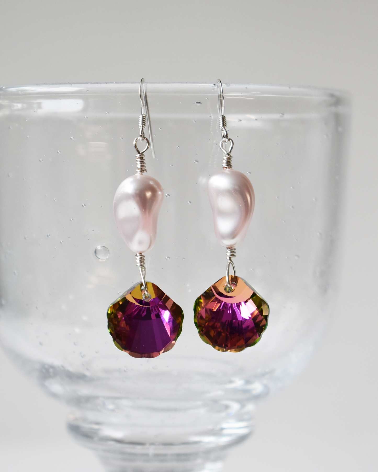 Pair of earrings with pink beads and purple gemstones on a clear stand.