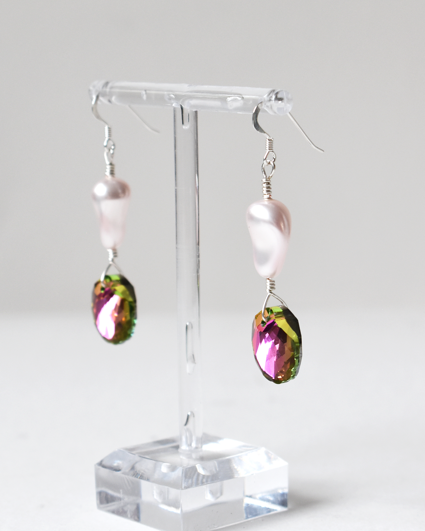 Pair of earrings with colorful teardrop-shaped beads on a clear stand against a white background
