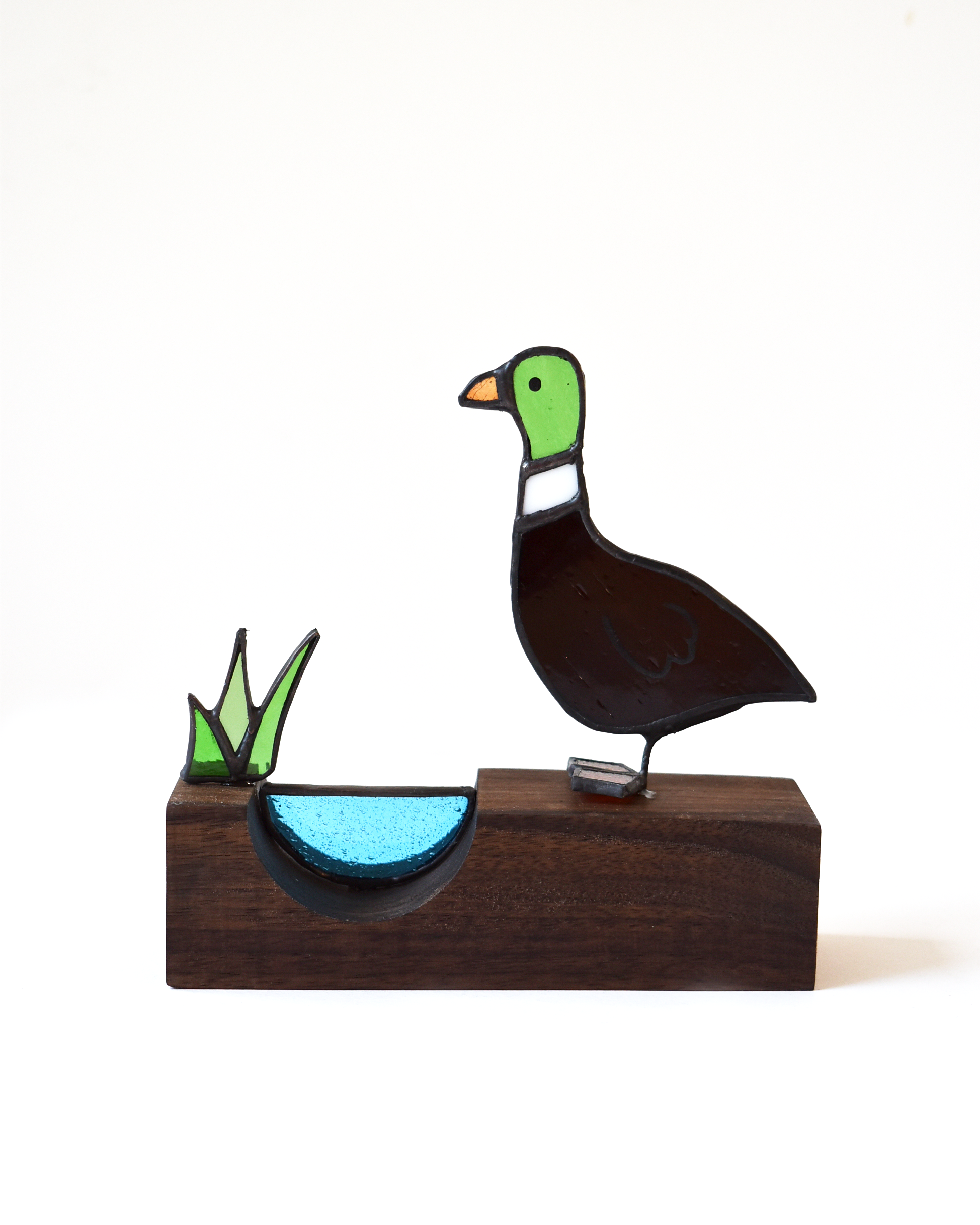 Decorative glass duck on a wooden base with a white background
