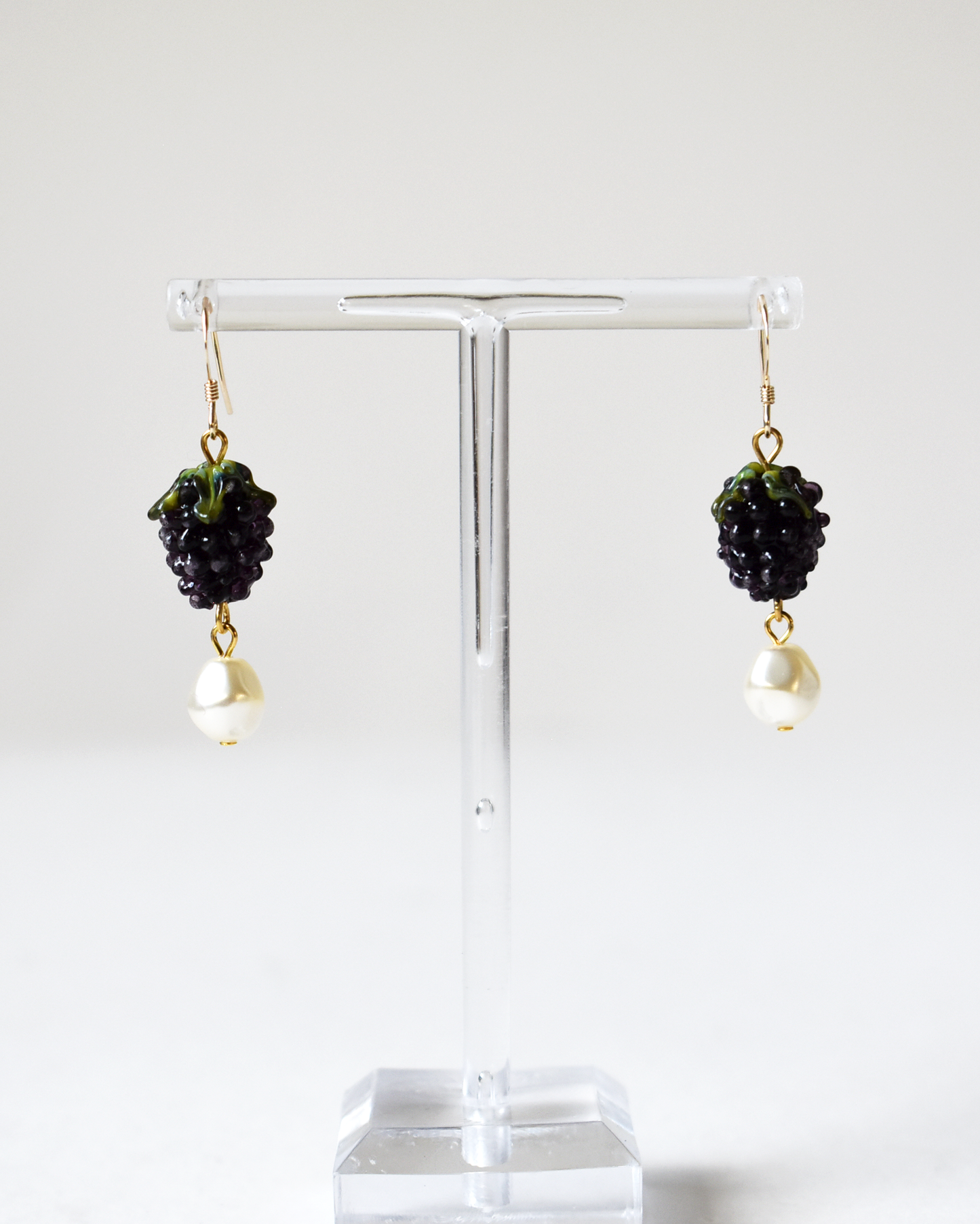 Pair of earrings with black and gold design on a clear stand against a white background