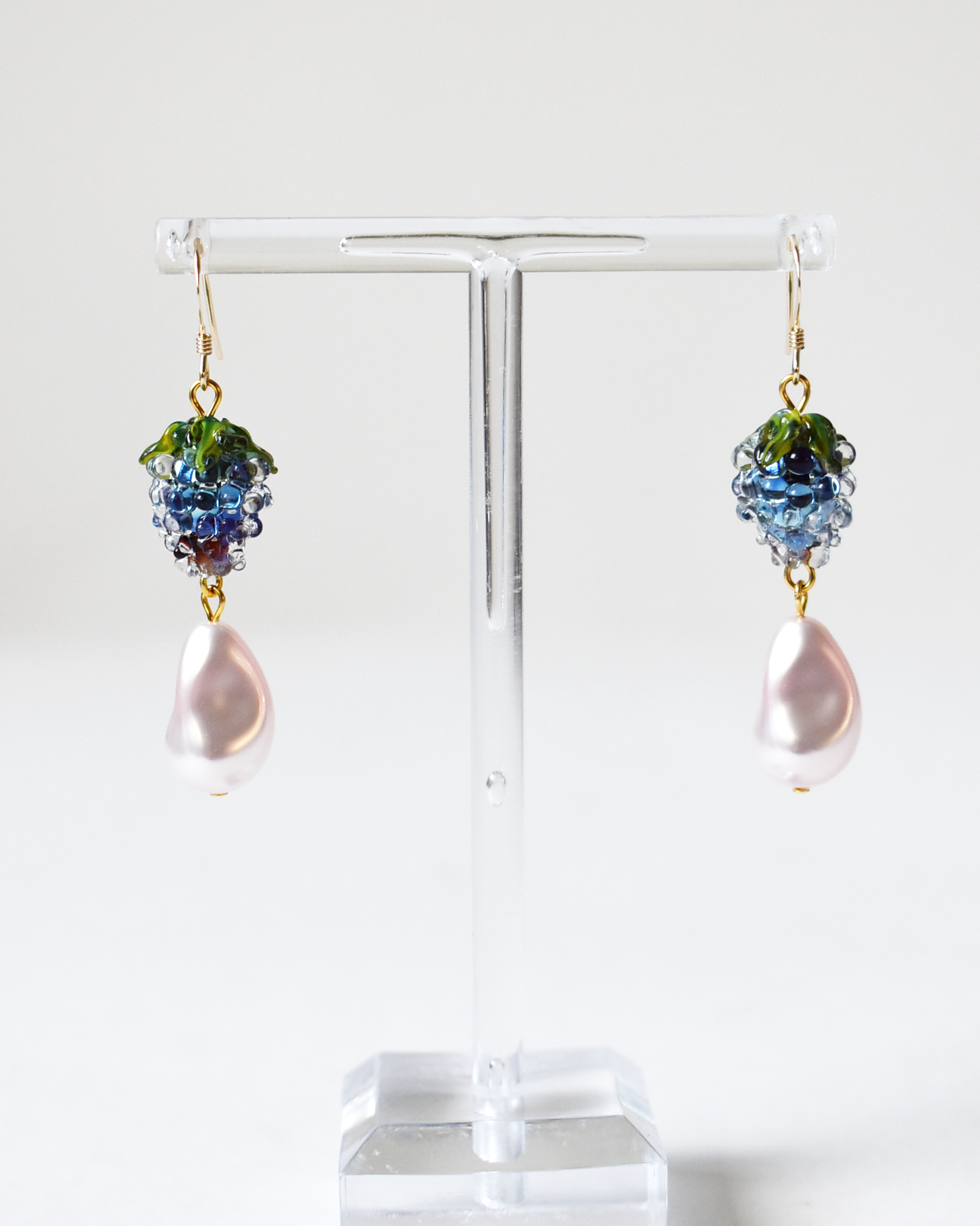 Pair of earrings with grape cluster design on a clear stand against a white background