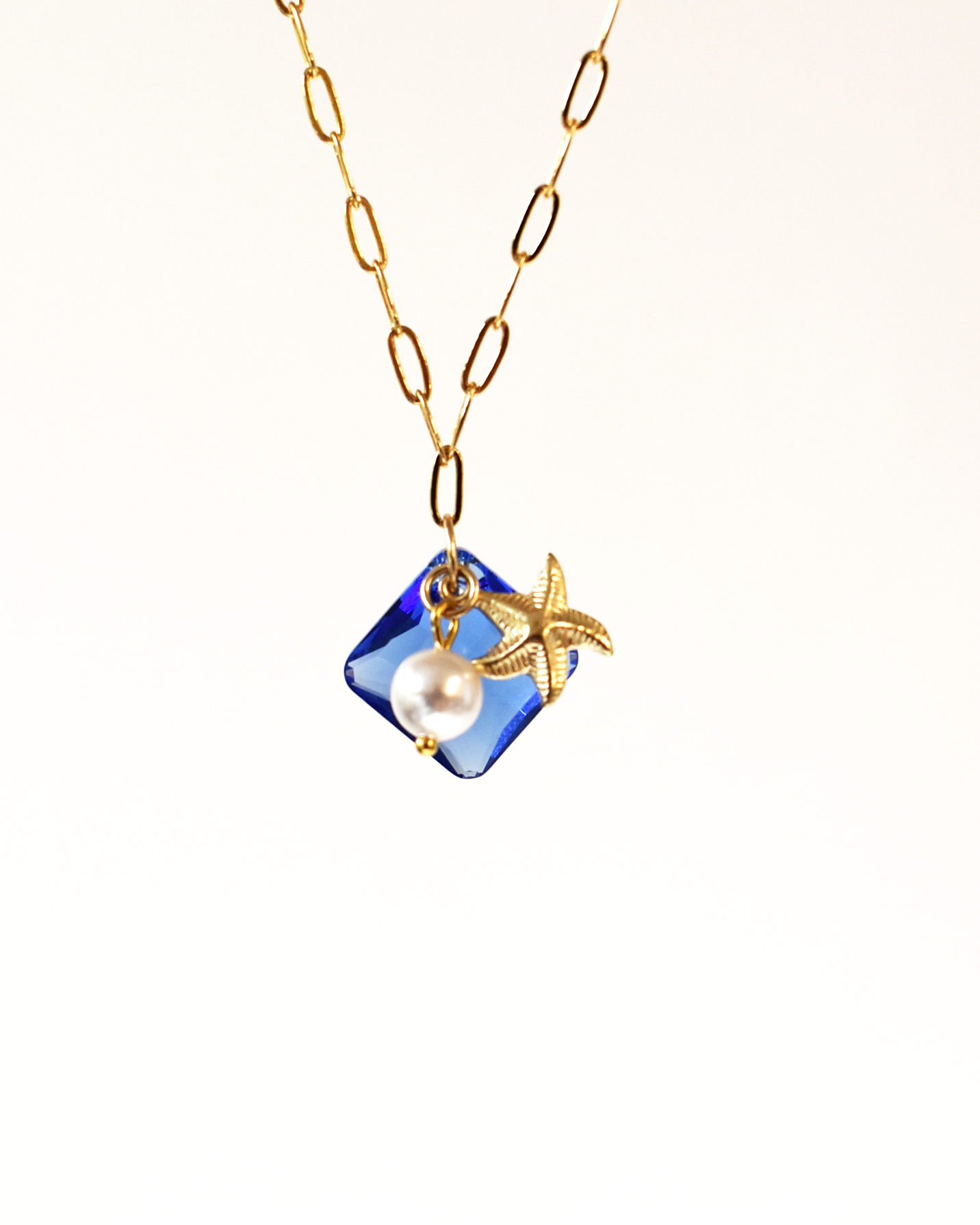 Gold necklace with a blue pendant featuring a pearl and leaf design on a white background