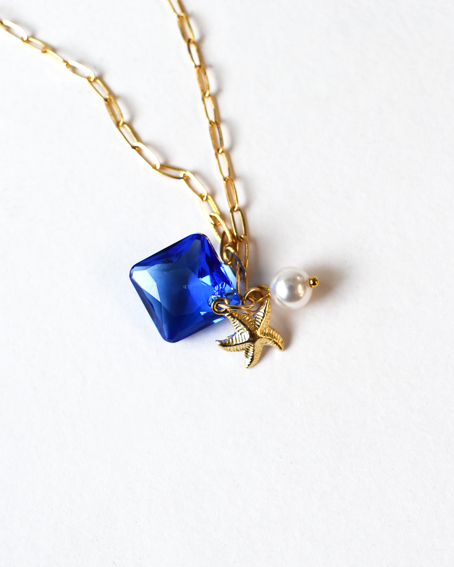Necklace with blue pendant, gold bird charm, and pearl on a white background