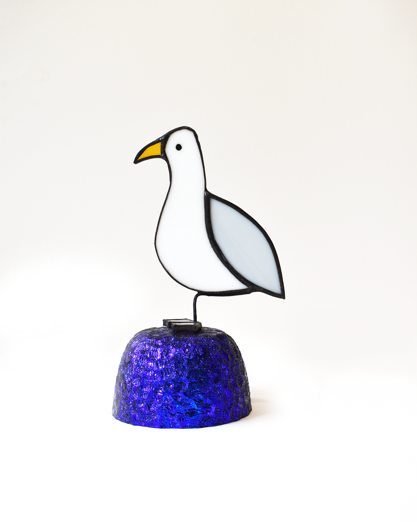 Stained glass seagull on a blue glittery base against a white background