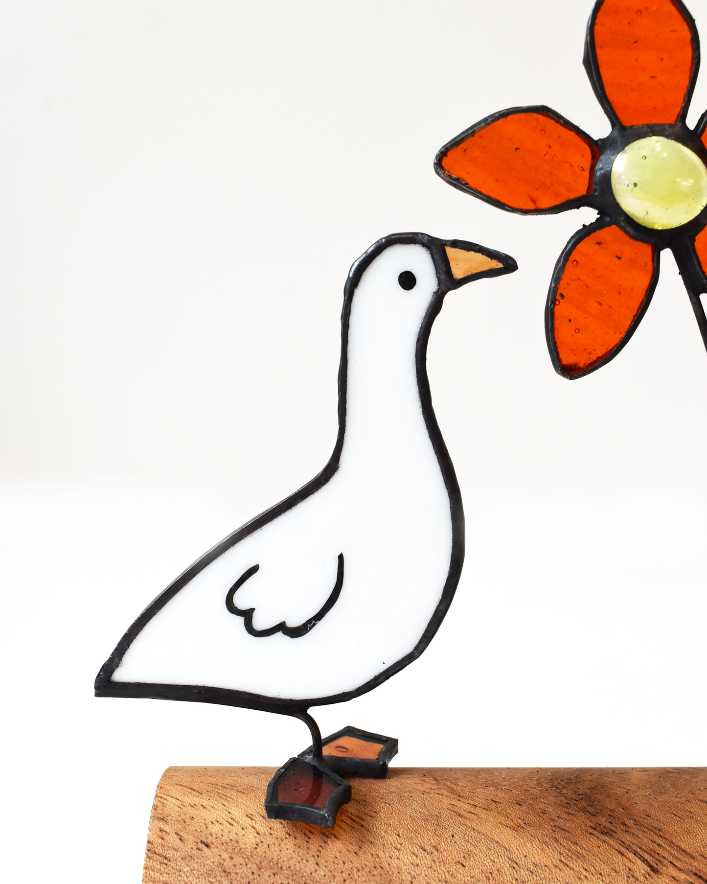 Decorative metal goose sculpture with a colorful flower on a wooden surface