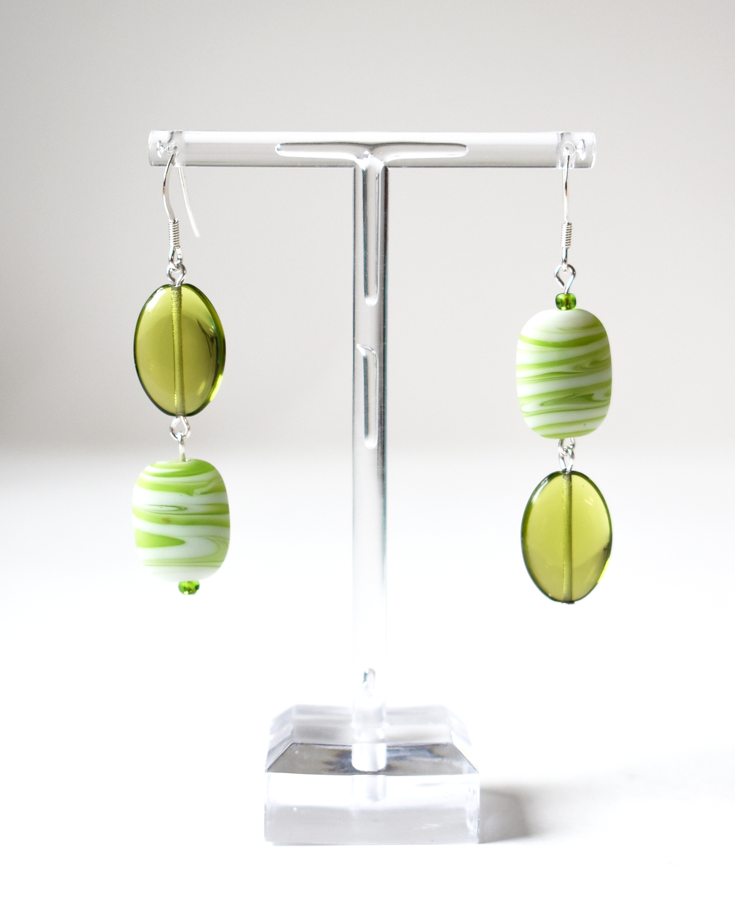 Green and white striped earrings on a white stand with a white background