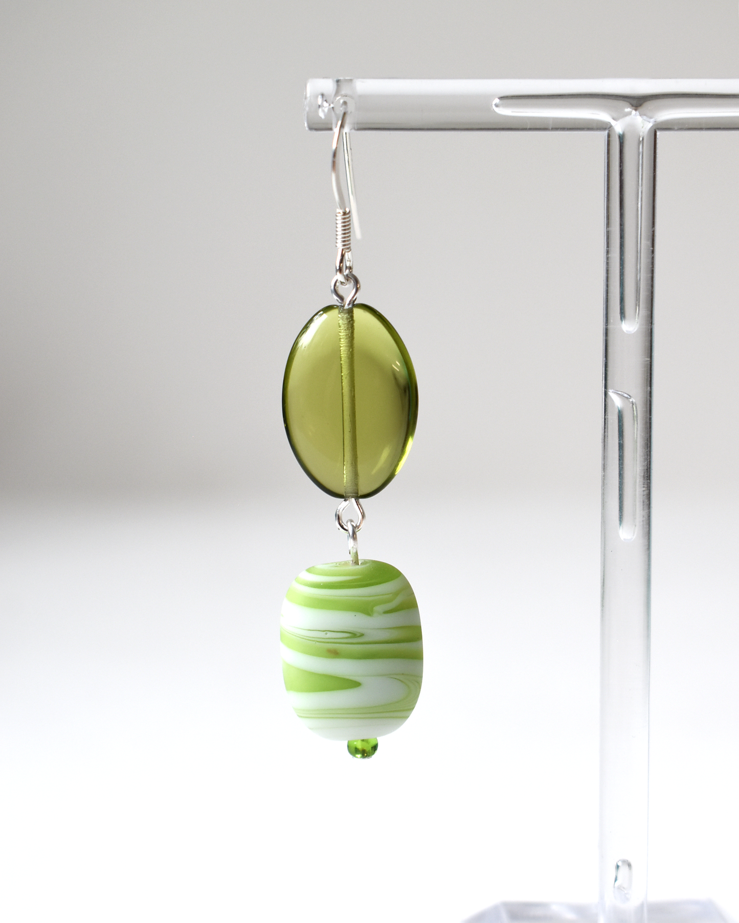 Green and white striped earrings on a clear stand against a white background