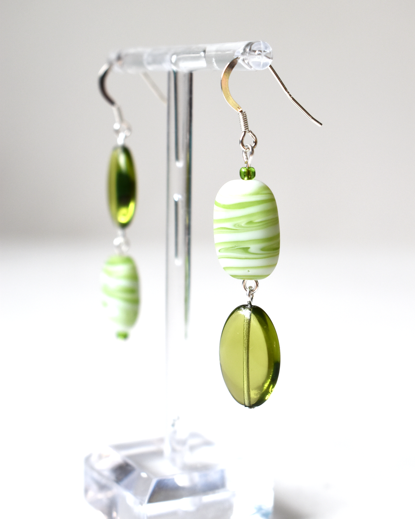 Green and white striped earrings on a clear stand against a white background