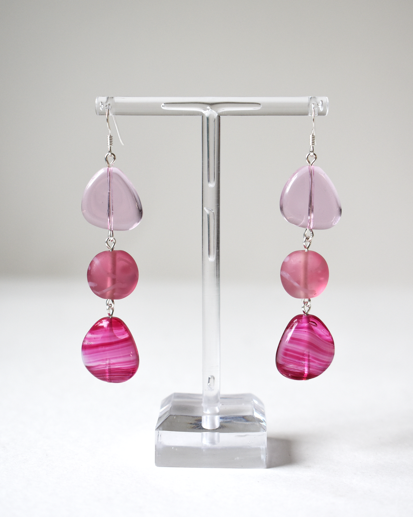 Pink teardrop earrings on a clear stand against a white background