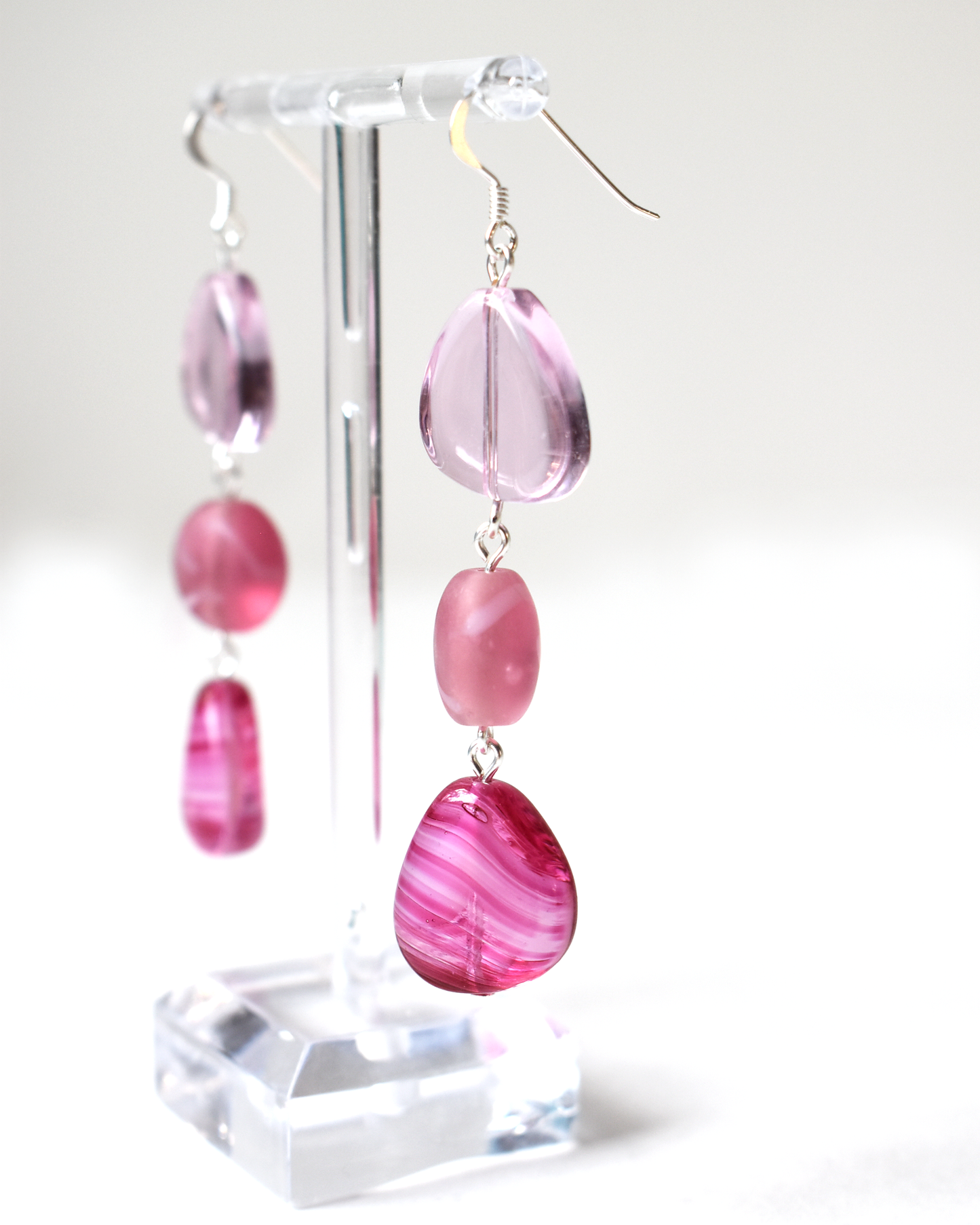 Pink teardrop and round bead earrings on a clear stand against a white background