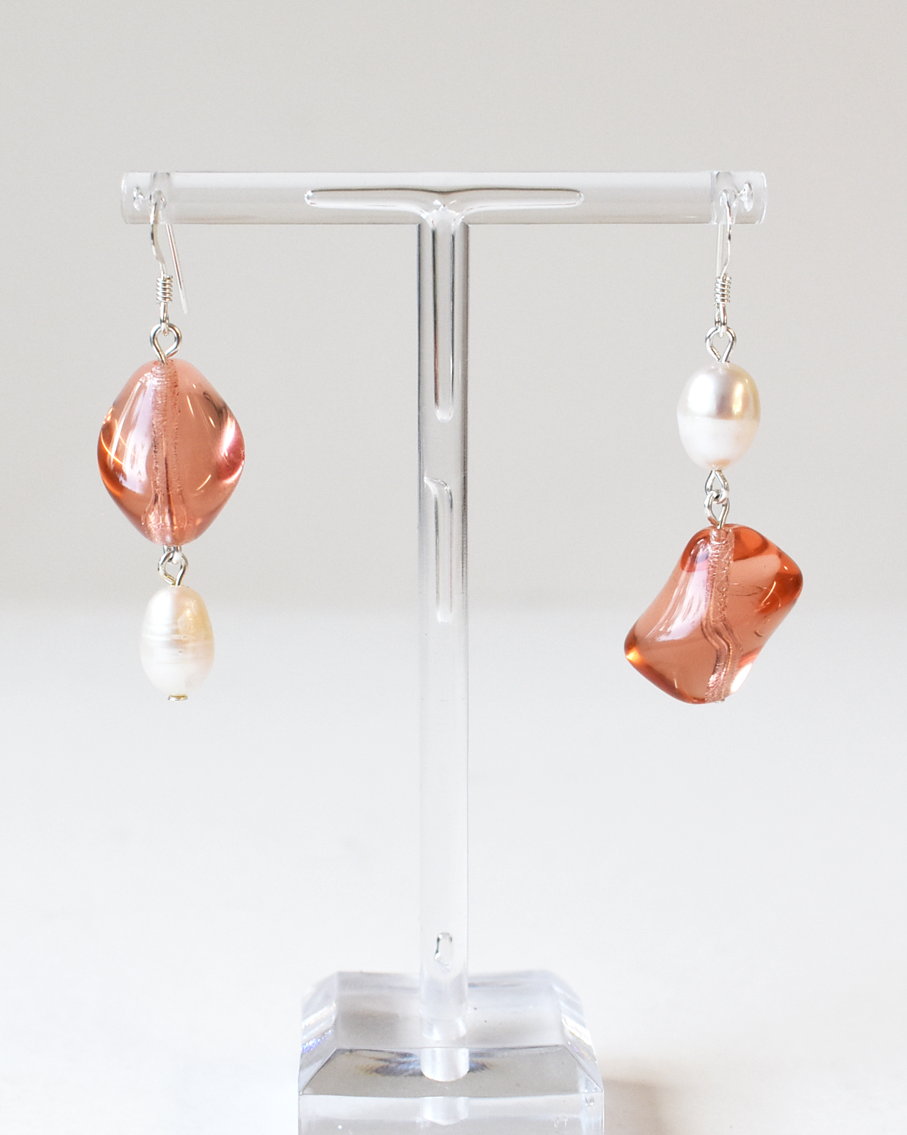 Pair of earrings with pink and white stones on a clear stand against a white background