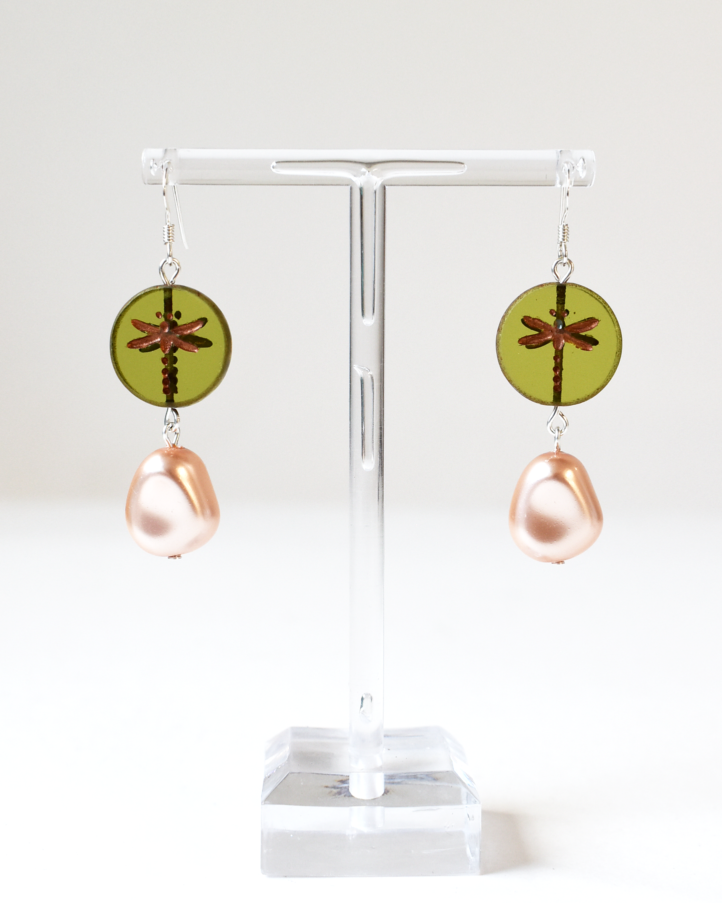 Pair of earrings with green circular and pink teardrop designs on a white stand.