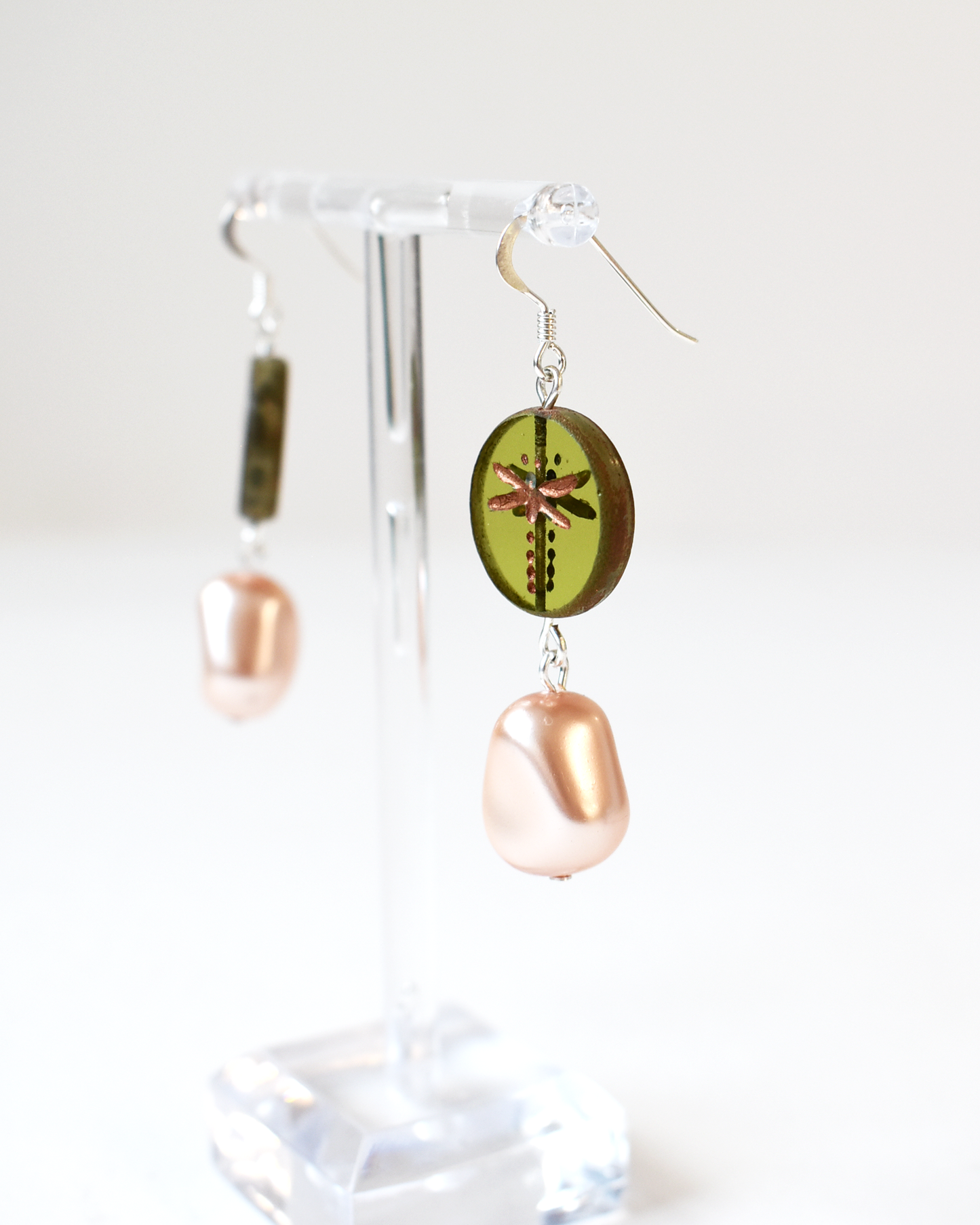 Pair of earrings with a green circular design and pinkish-beige dangling elements on a clear stand.