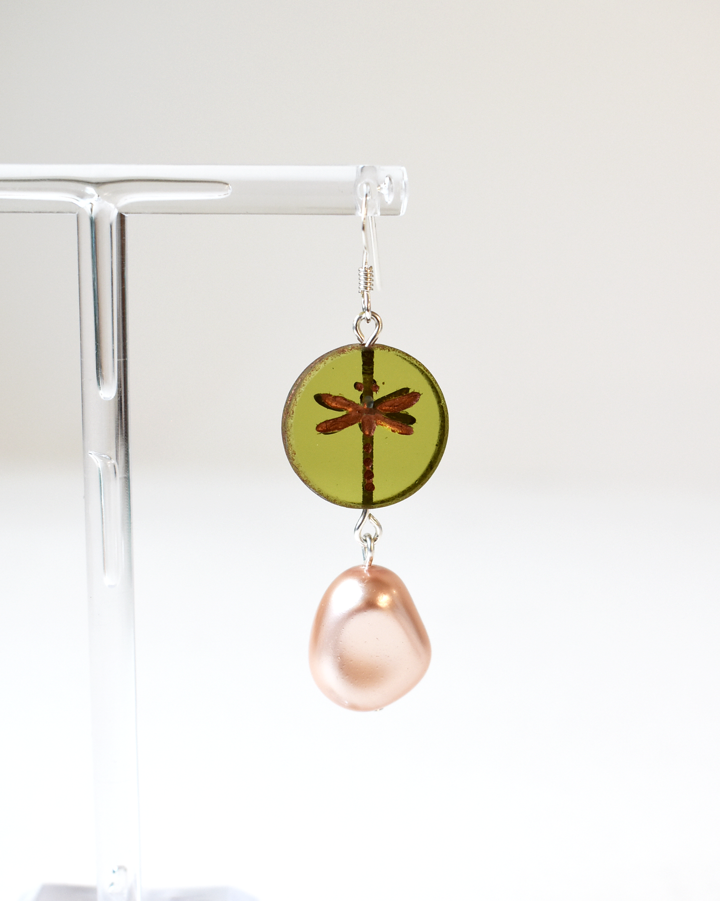 Earring with green round pendant and pink teardrop on a clear stand