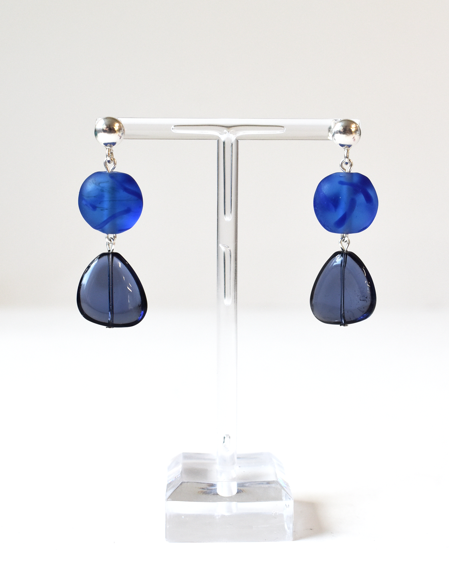 Blue teardrop earrings on a clear stand against a white background