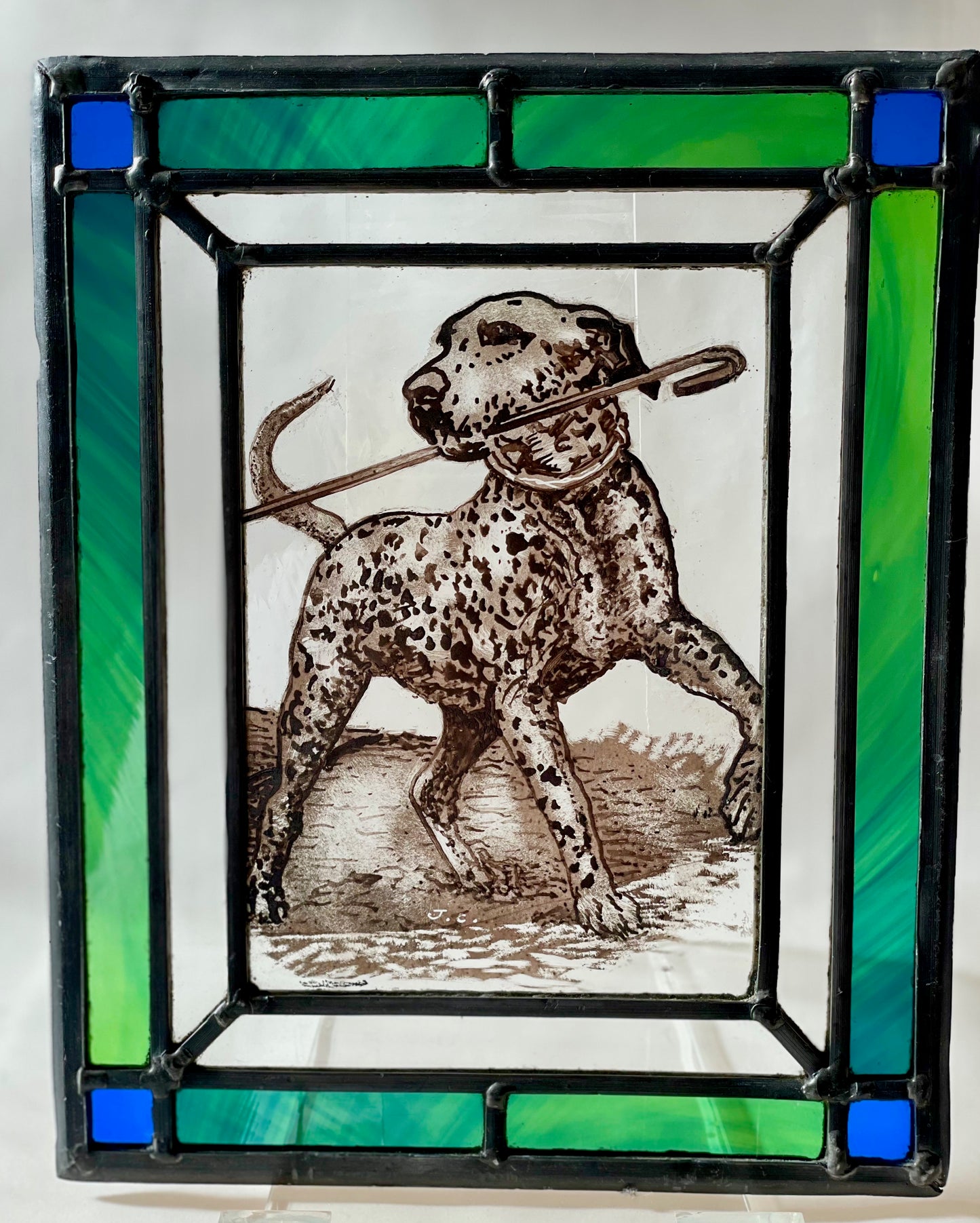 hand painted and kiln fired stained glass panel with an image of a dapper dog green and blue glass to the border