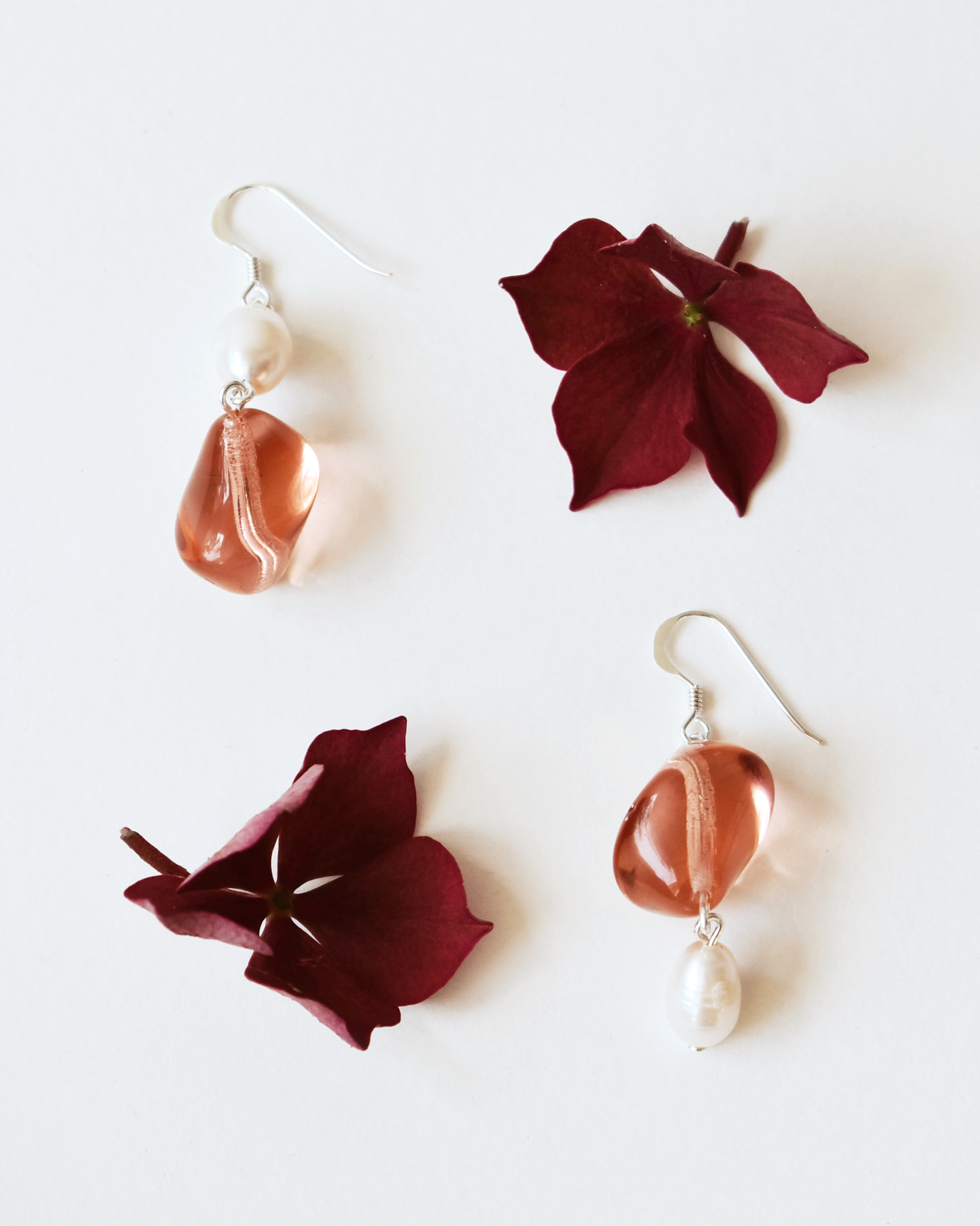 Pair of earrings with maroon flower-like pendants and copper-colored stones on a white background