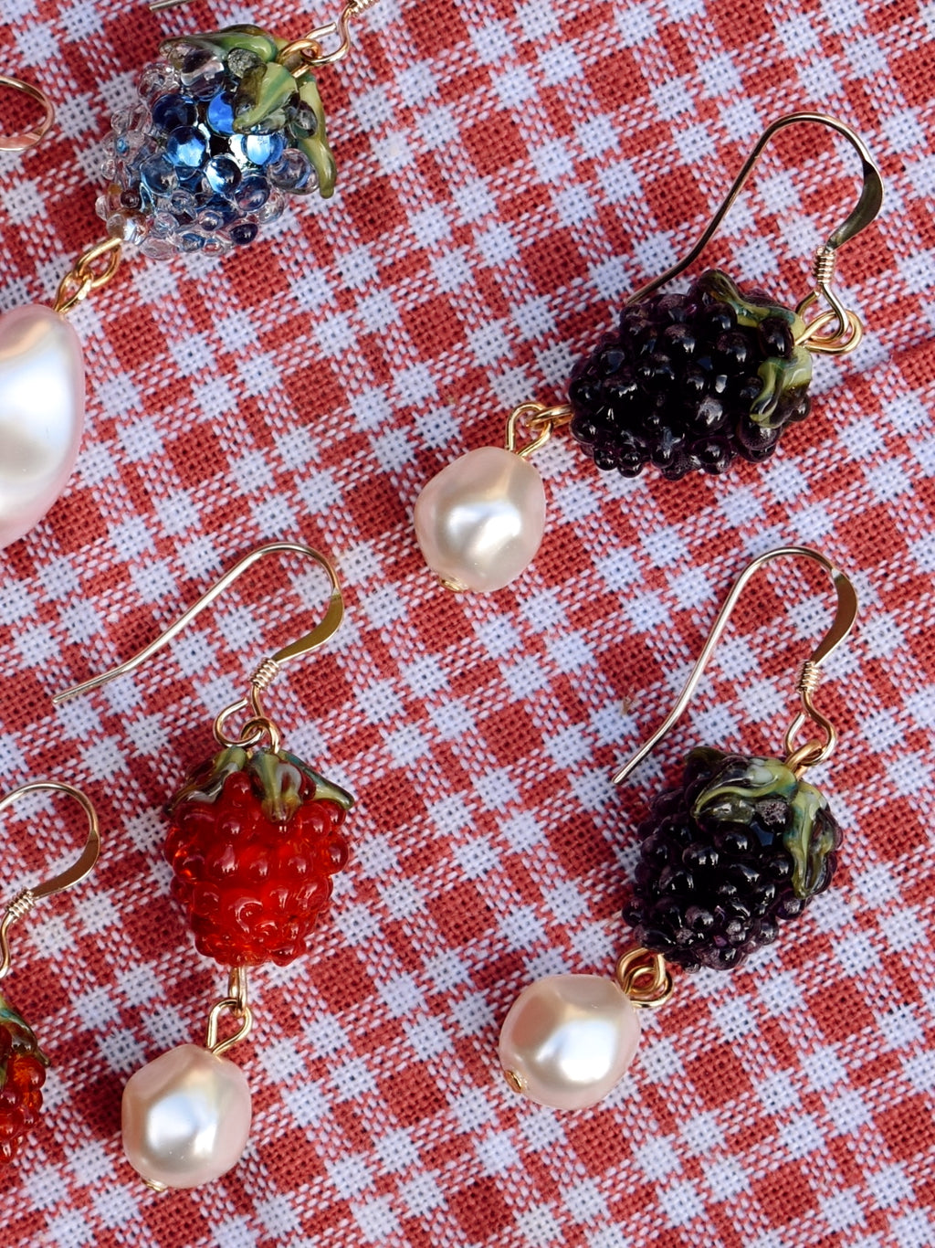 Earrings with berry and pearl designs on a red and white checkered background