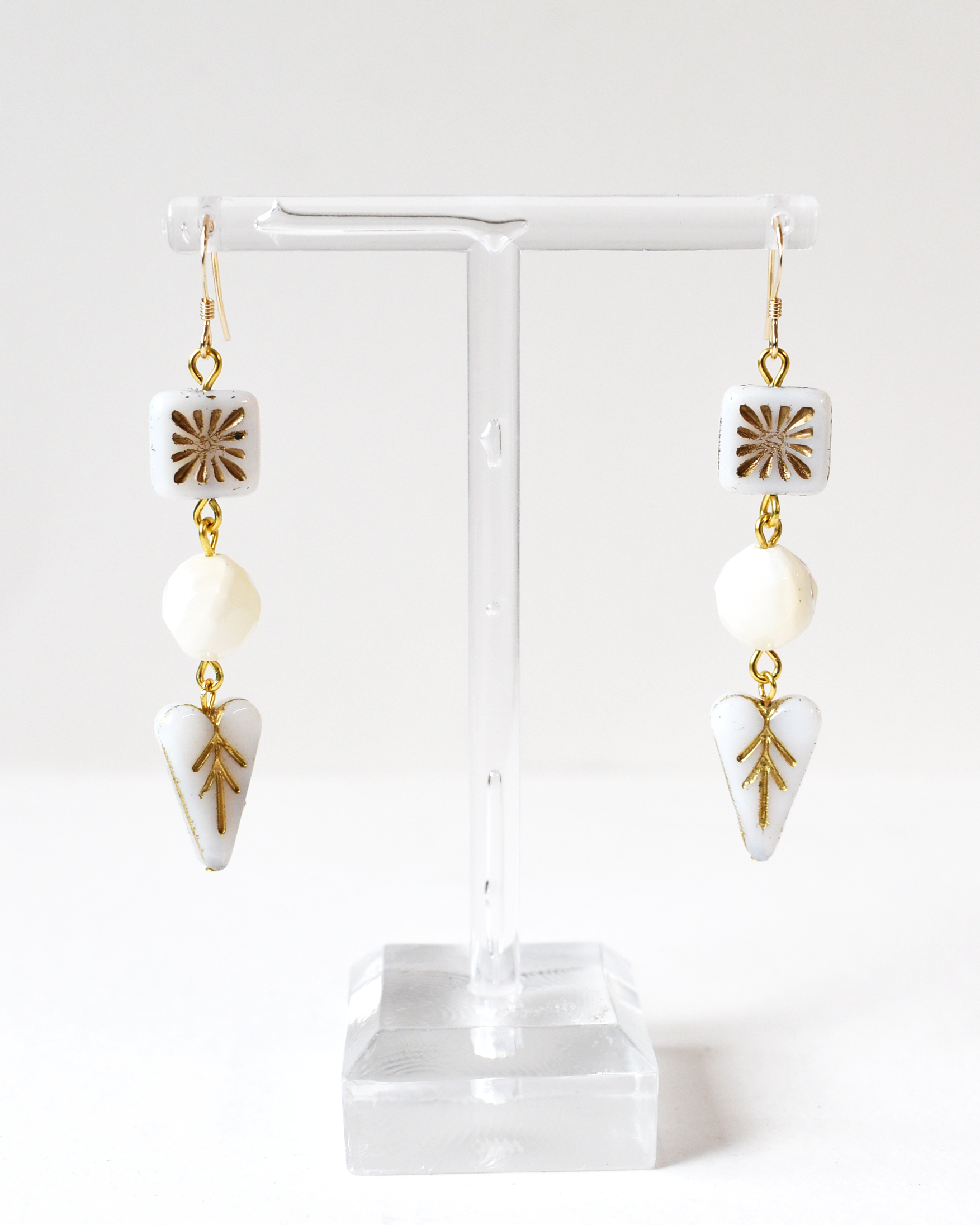 Pair of earrings with gold accents and white stones on a clear stand against a white background