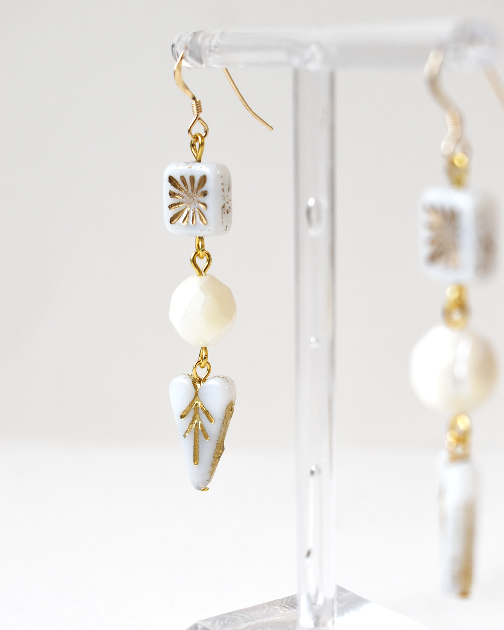 White and gold earrings on a clear stand against a white background