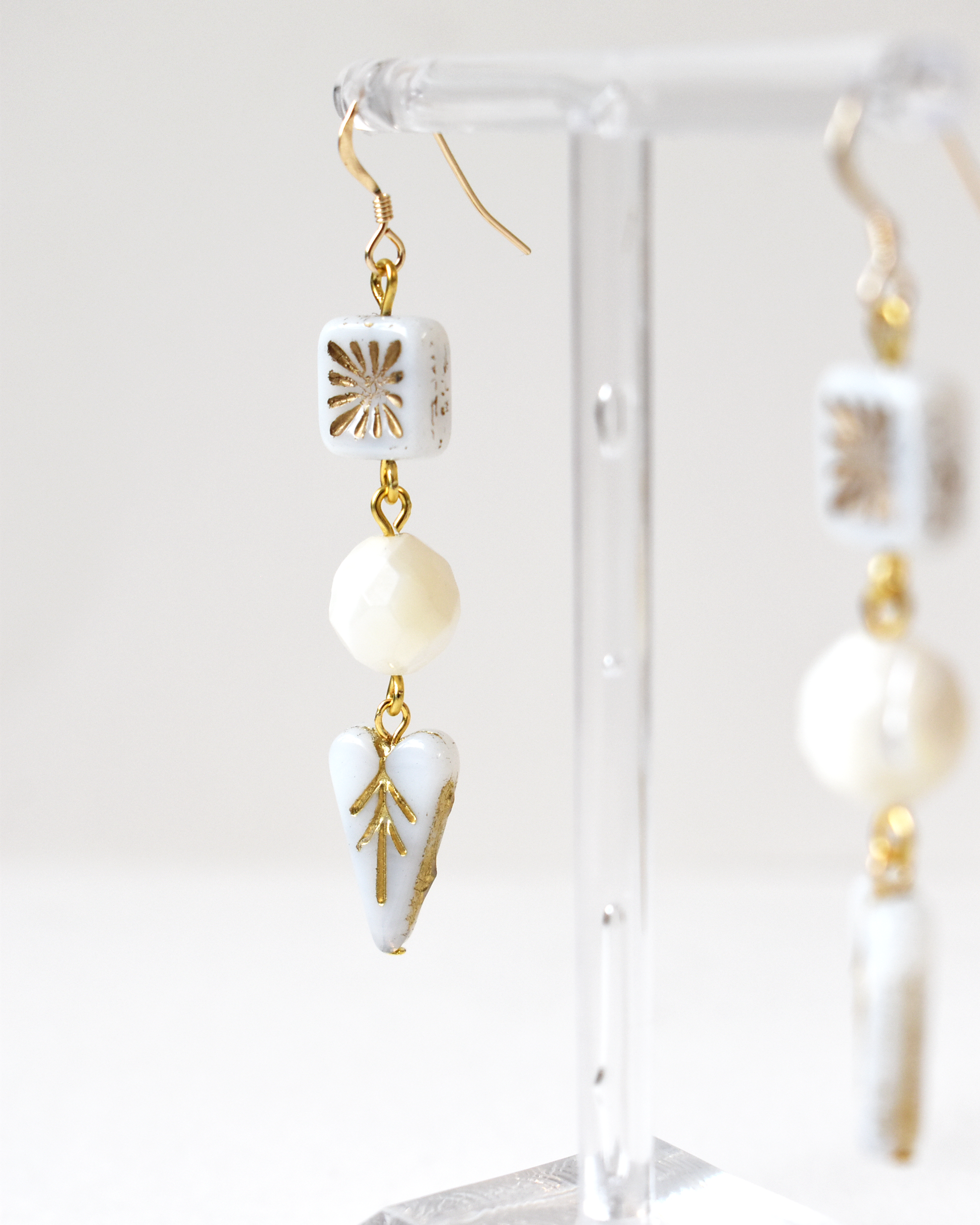White and gold earrings on a clear stand against a white background