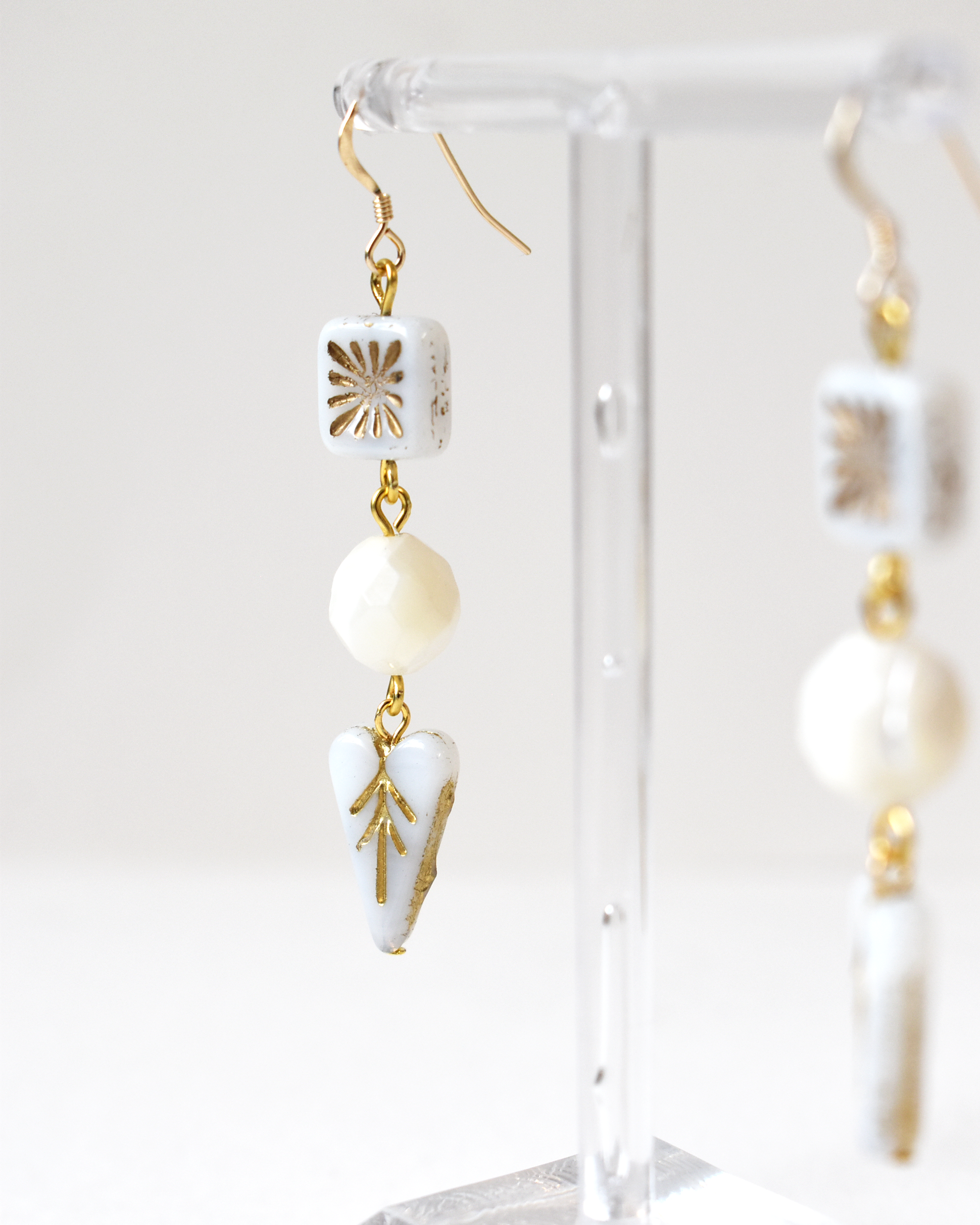 White and gold earrings on a clear stand against a white background