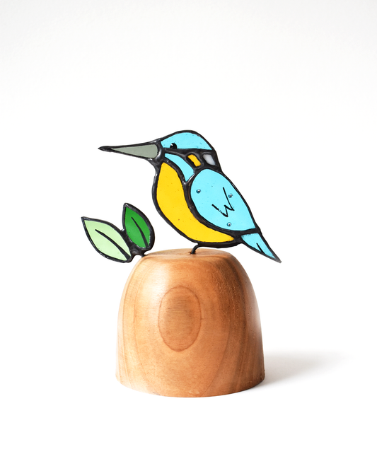 Colorful bird figurine on a wooden base with leaves against a white background