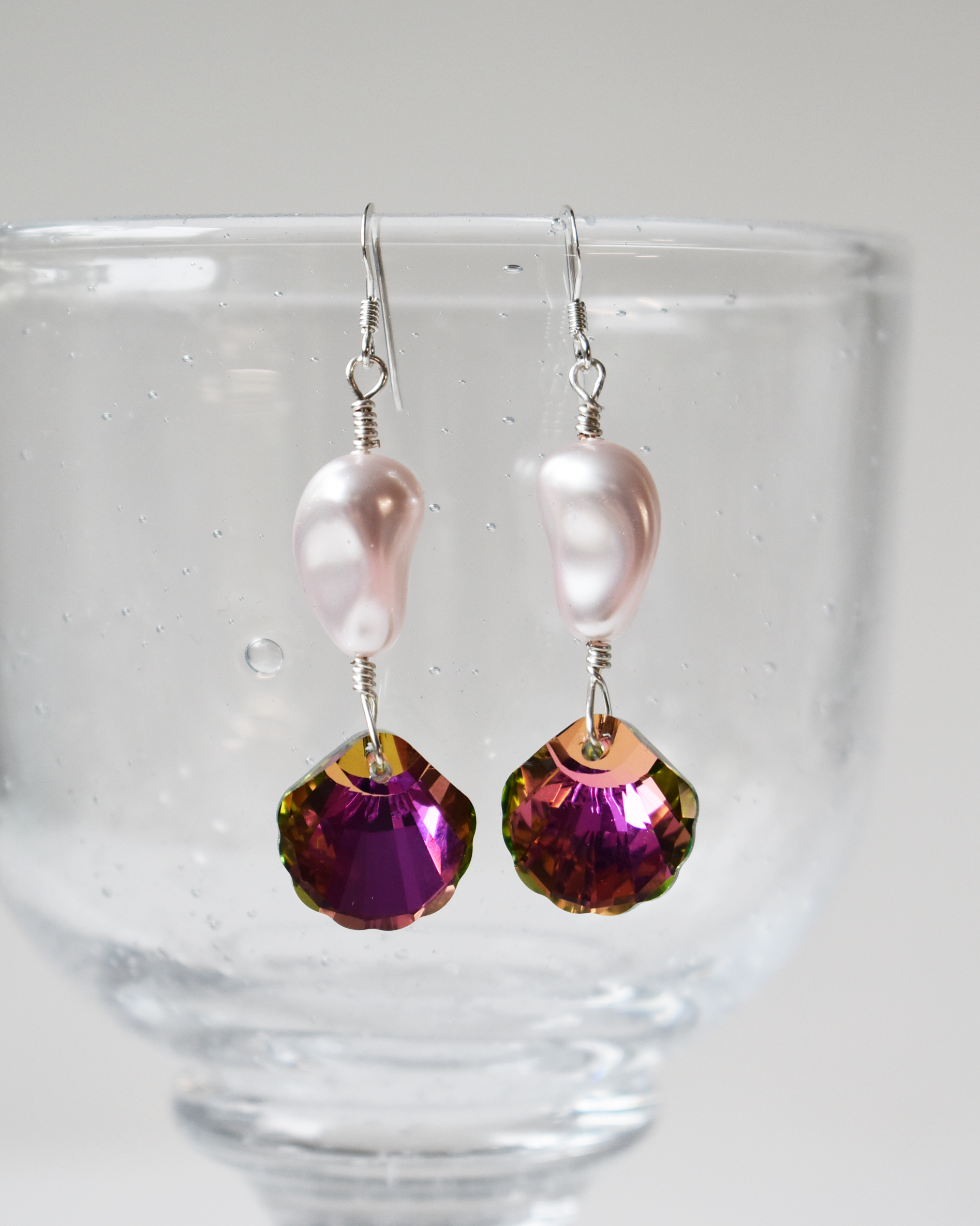 Pair of earrings with pink beads and purple gemstones on a clear stand.