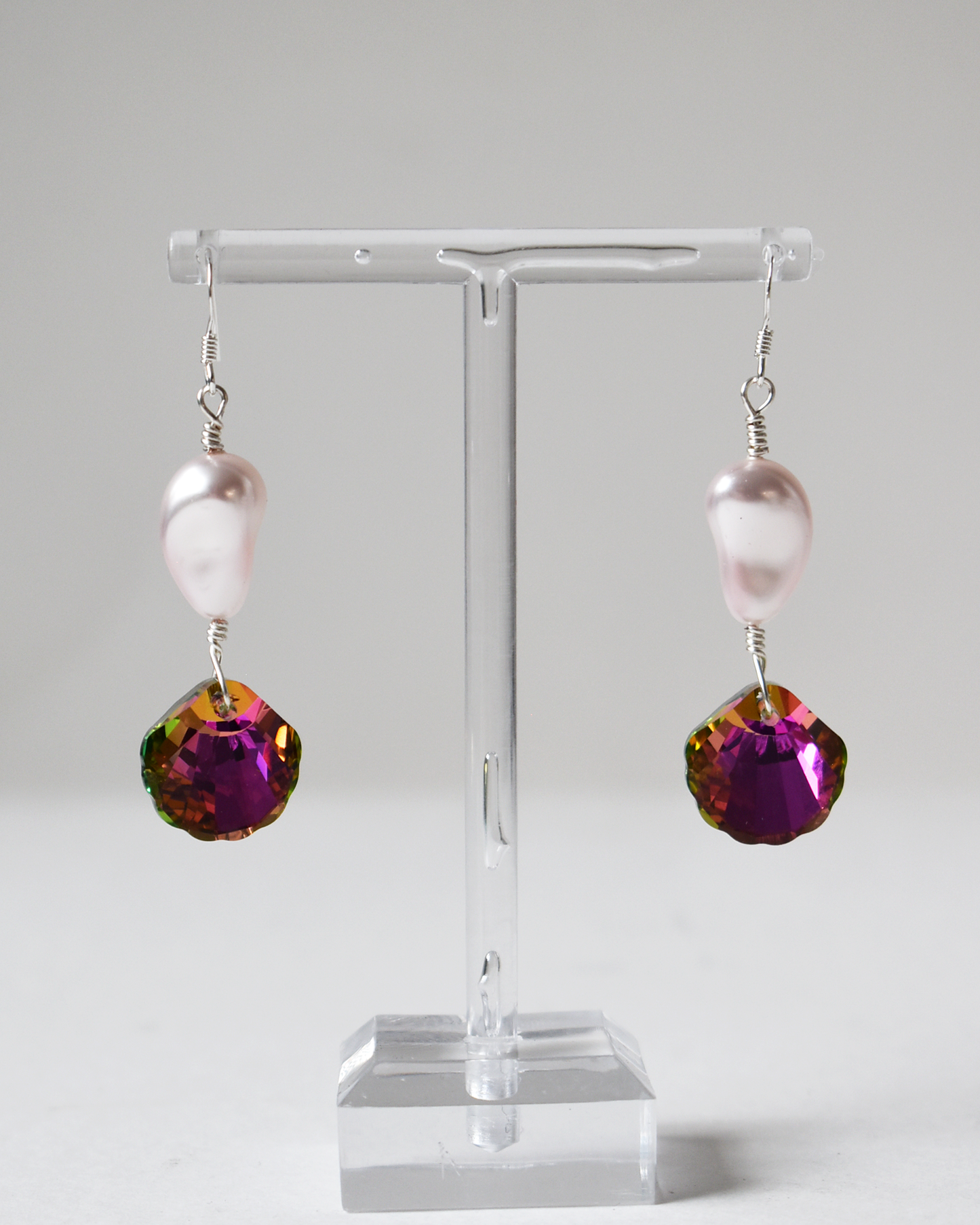Pair of earrings with pink pearls and purple gemstones on a clear stand against a white background