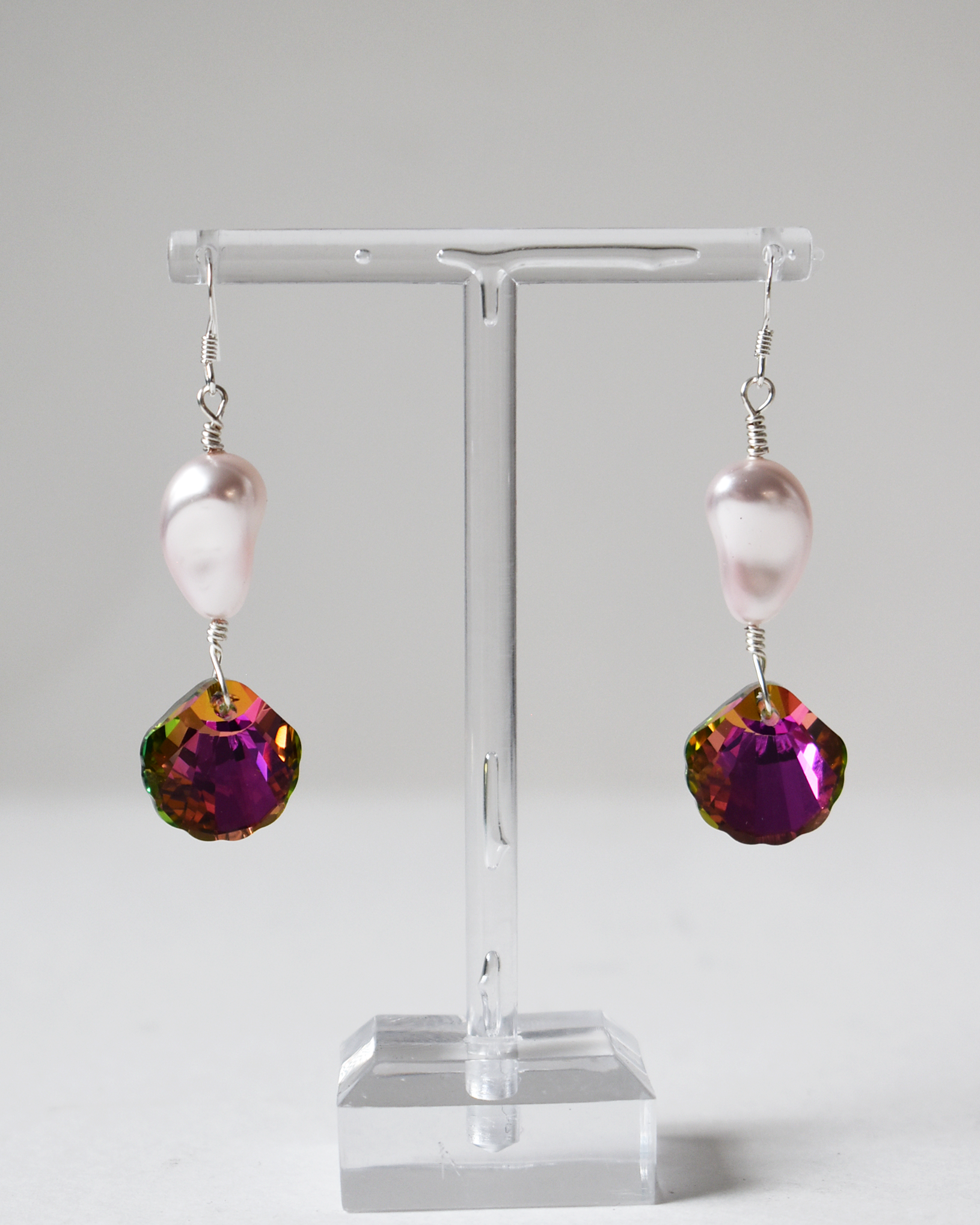 Pair of earrings with pink pearls and purple gemstones on a clear stand against a white background