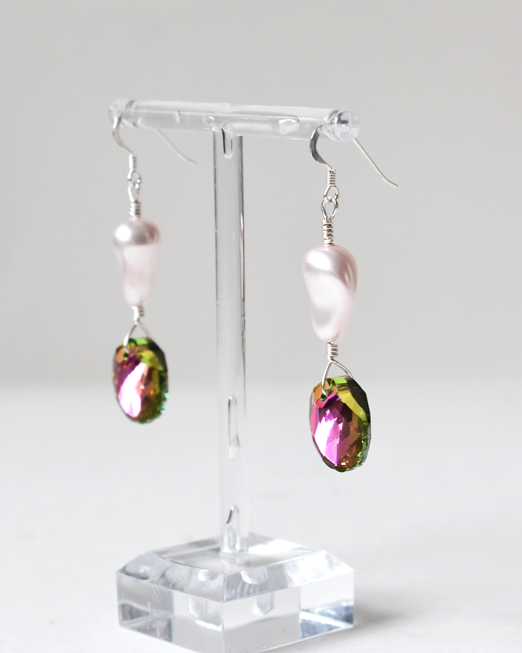 Pair of earrings with colorful teardrop-shaped beads on a clear stand against a white background