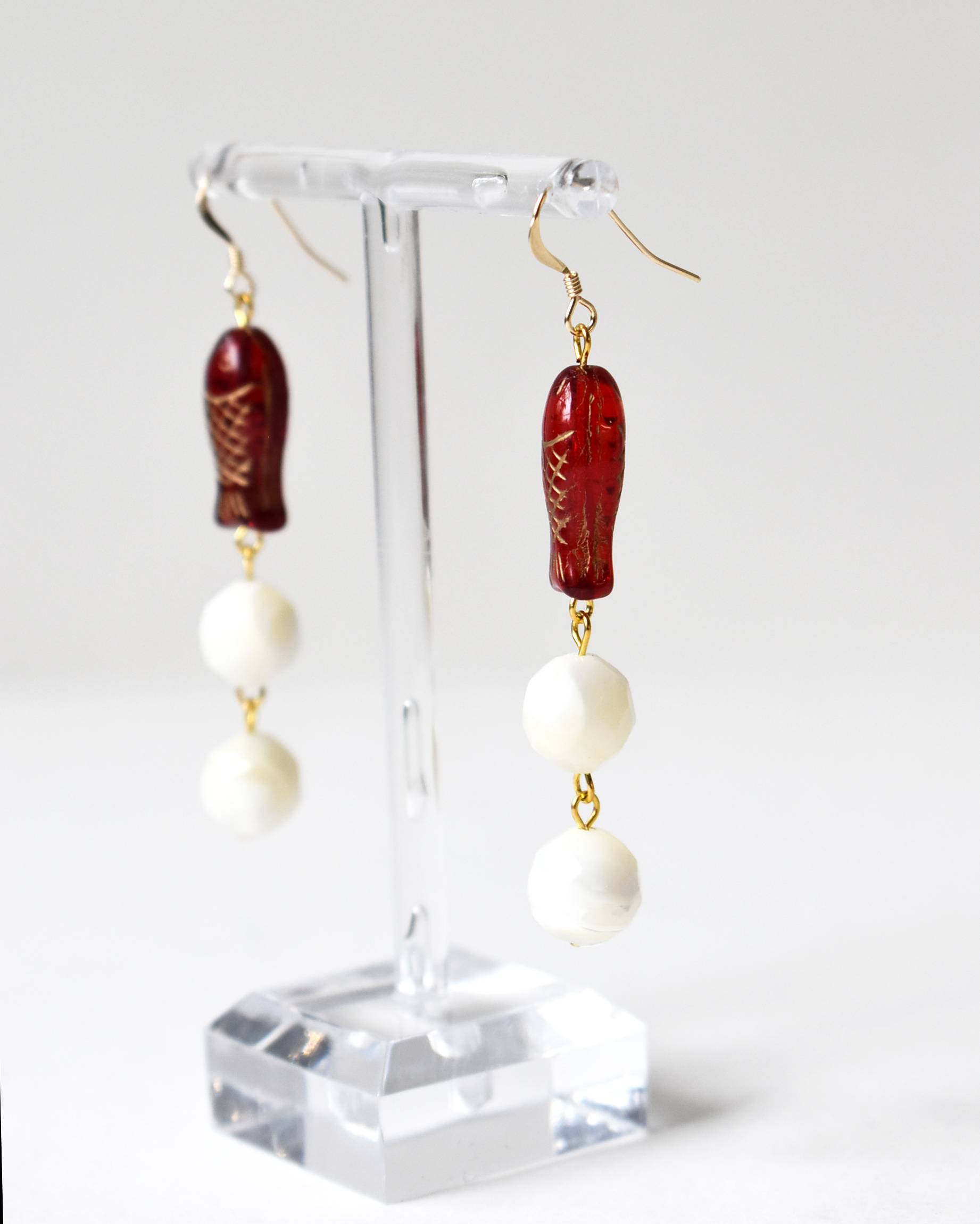 Pair of earrings with red and white beads on a clear stand against a white background