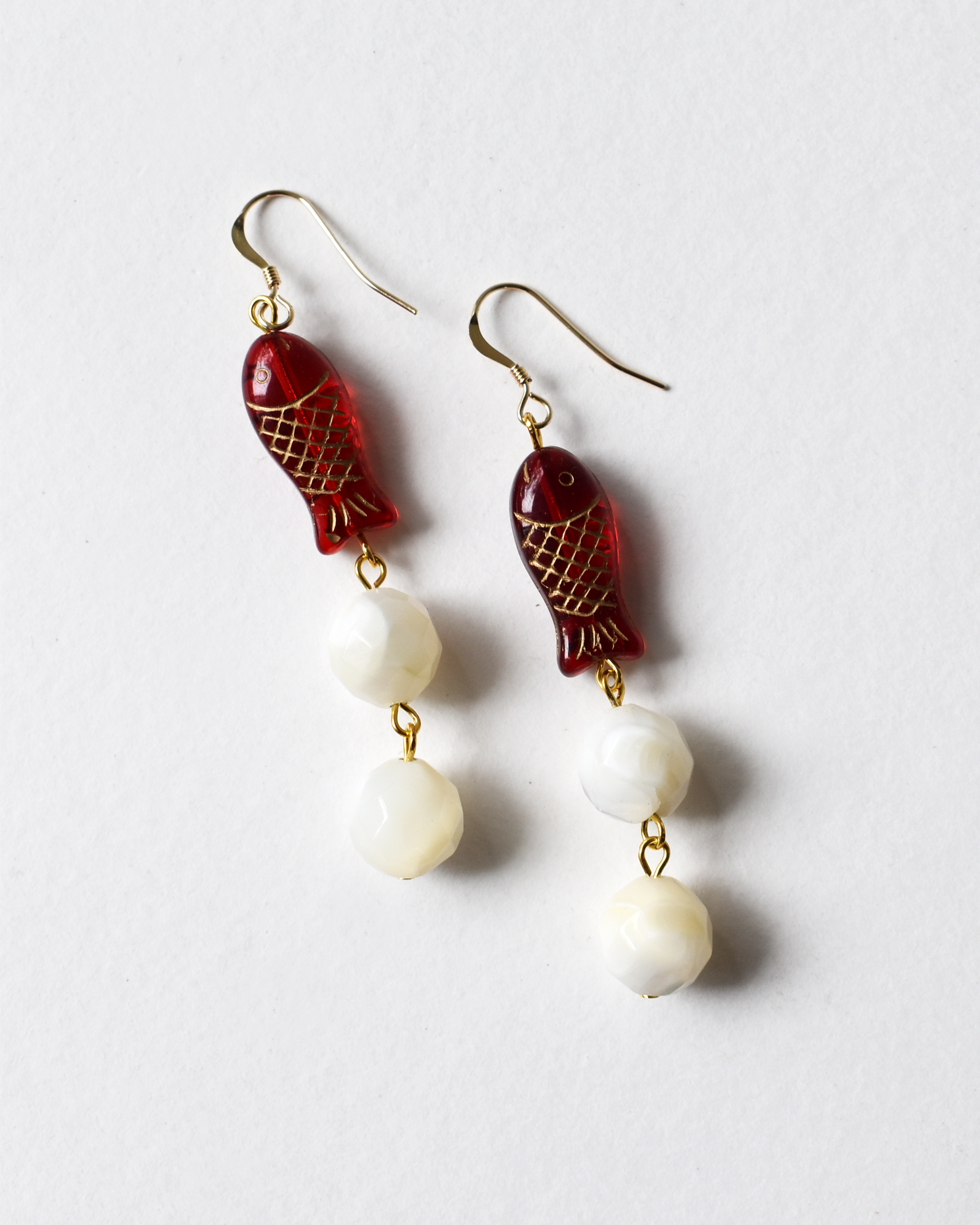 Pair of earrings with red fish-shaped charms and white beads on a light gray background