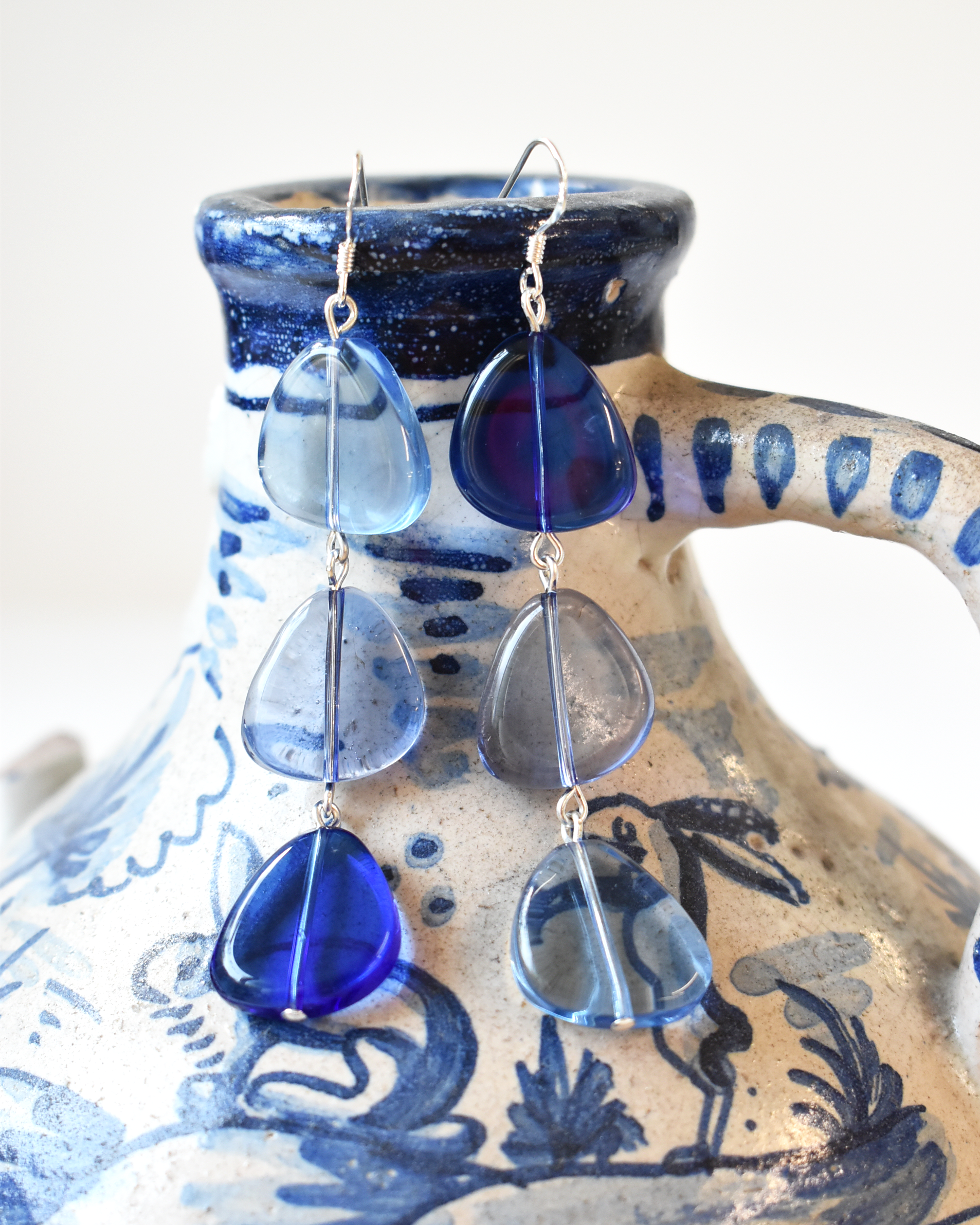 Blue teardrop-shaped earrings on a ceramic holder with blue and white design.