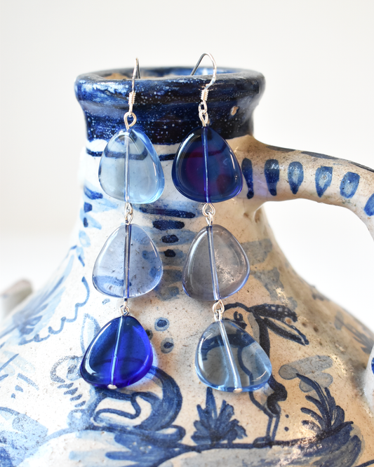 Blue teardrop-shaped earrings on a ceramic holder with blue and white design.