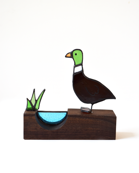 Decorative glass duck on a wooden base with a white background