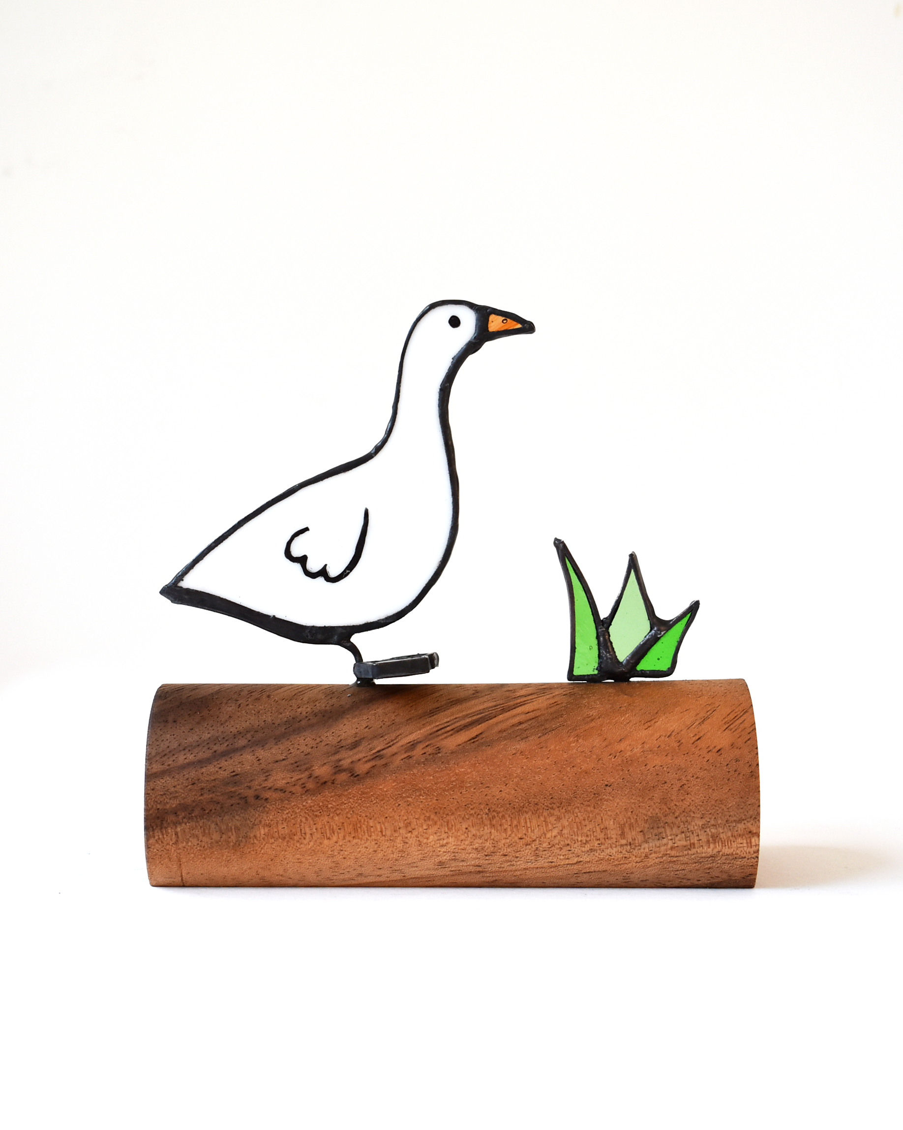 Decorative goose figure on a wooden base with grass detail against a white background
