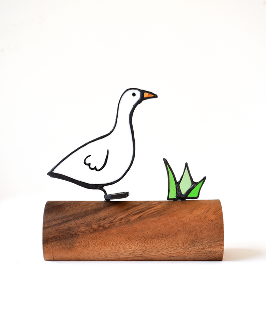 Decorative goose figure on a wooden base with grass detail against a white background