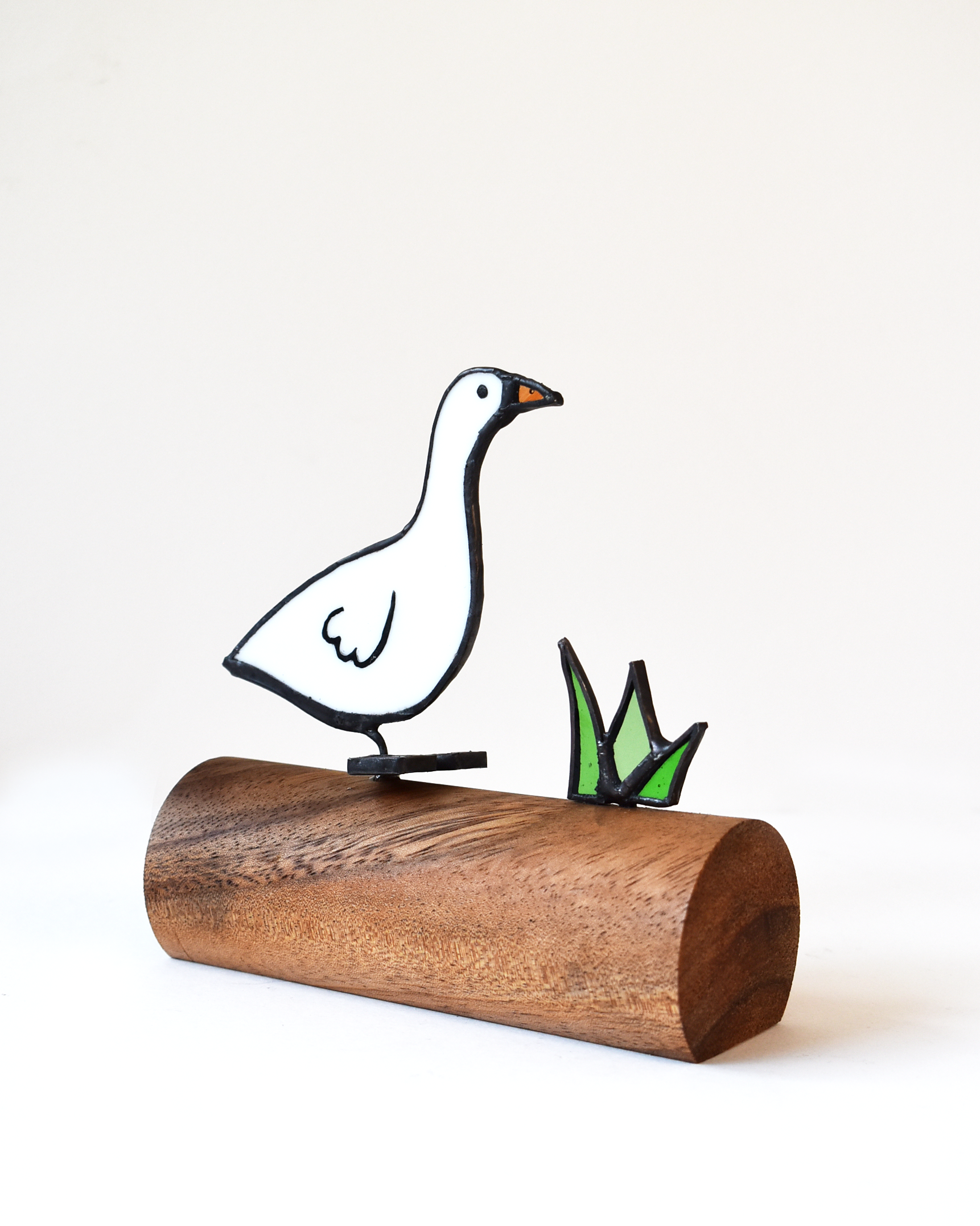 Decorative goose figure on a wooden base with grass on a white background