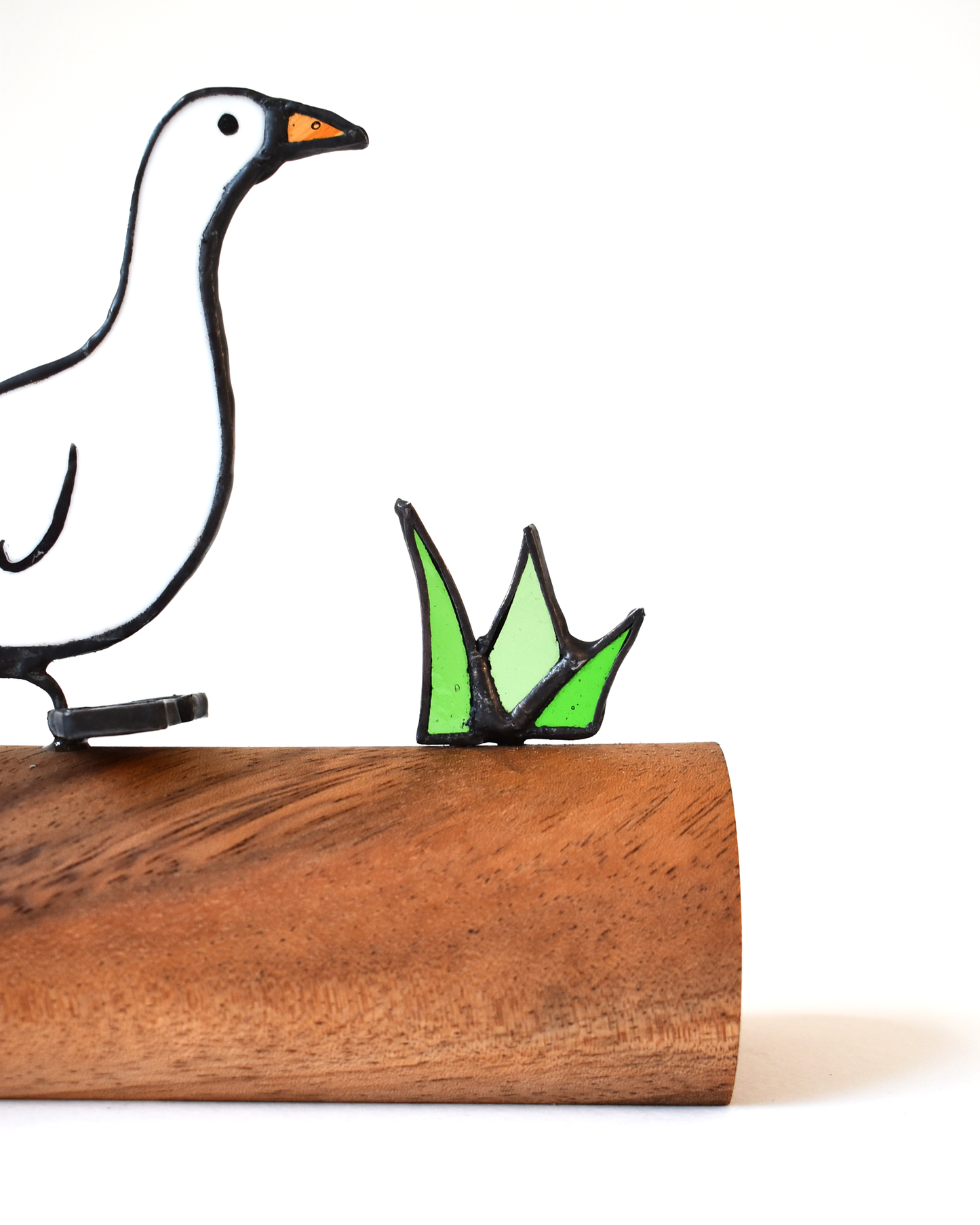 Decorative goose figure on a wooden log with a smaller green goose figure beside it.
