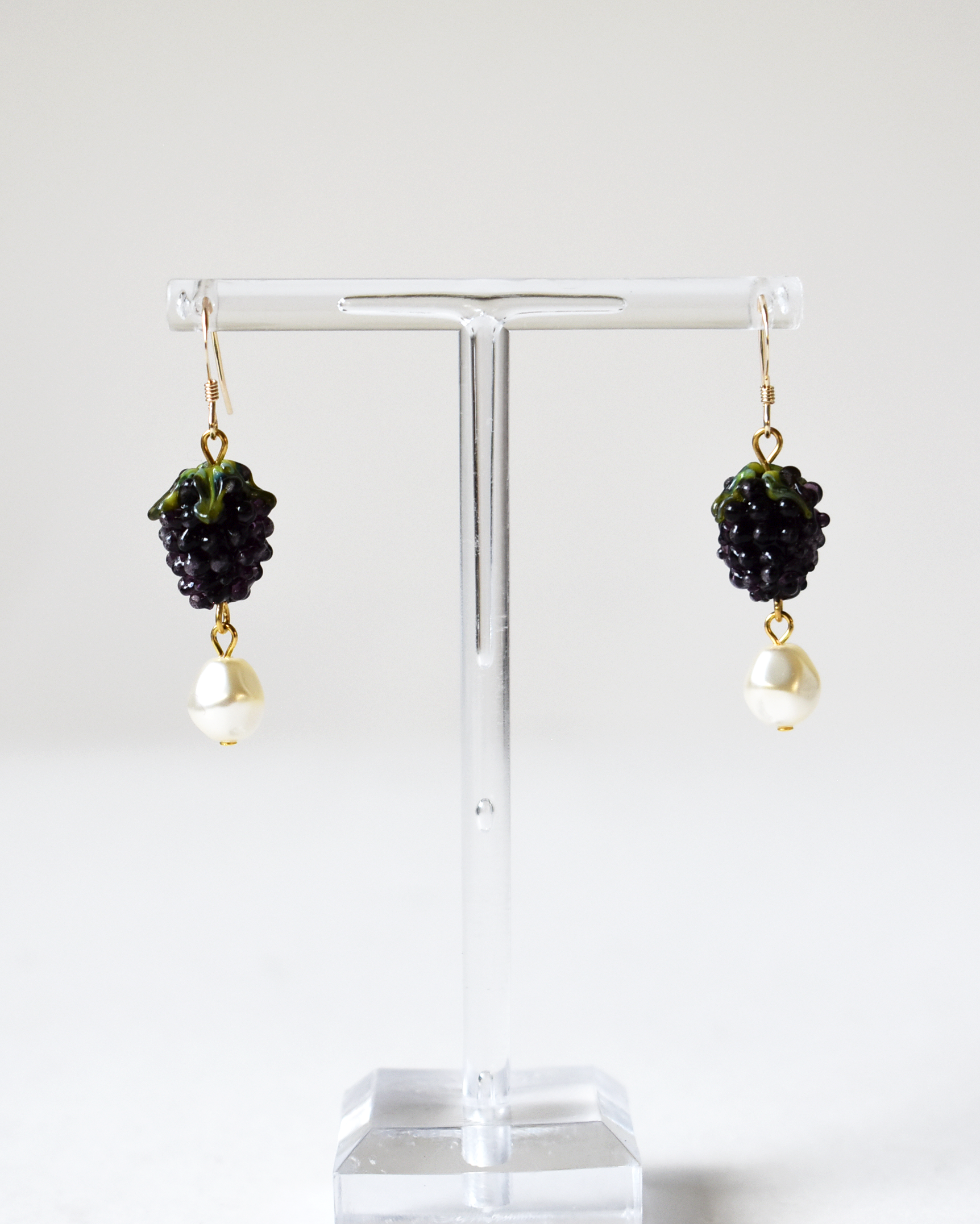Pair of earrings with black and gold design on a clear stand against a white background