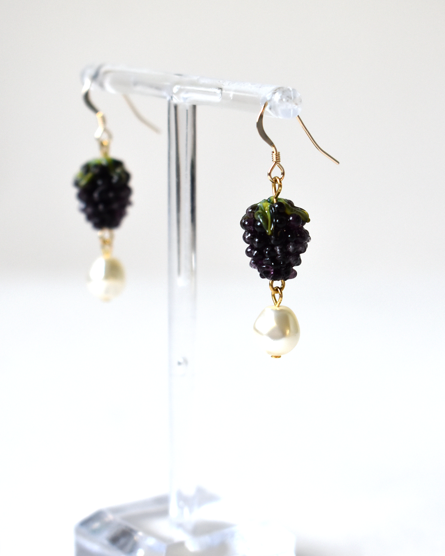 Black berry earrings on a clear stand against a white background