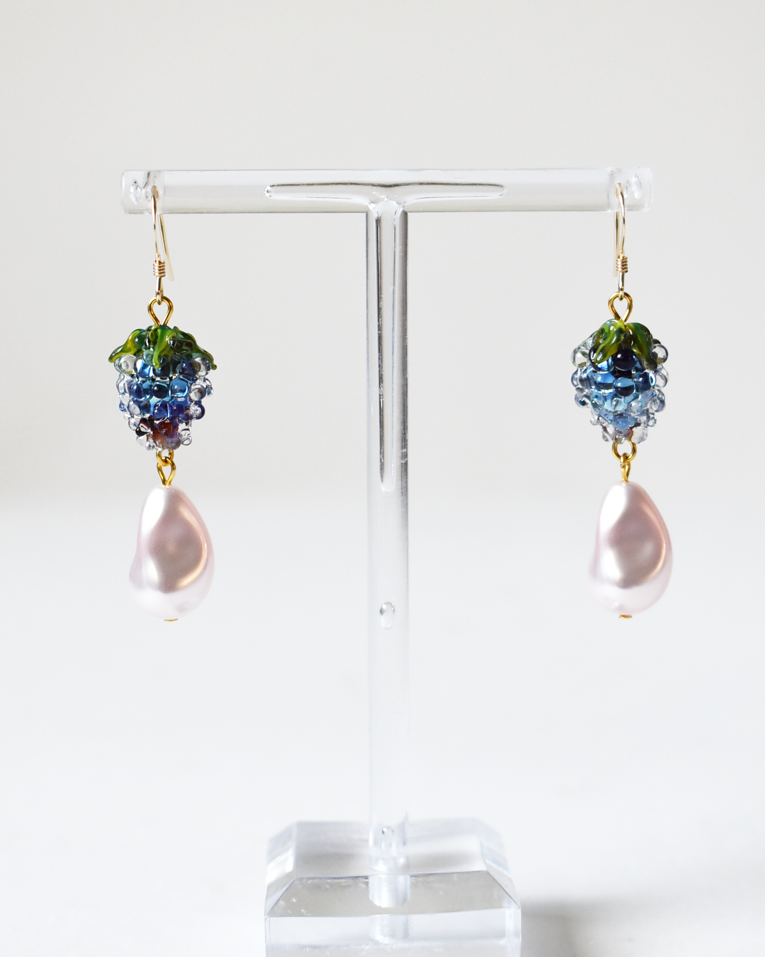 Pair of earrings with grape cluster design on a clear stand against a white background