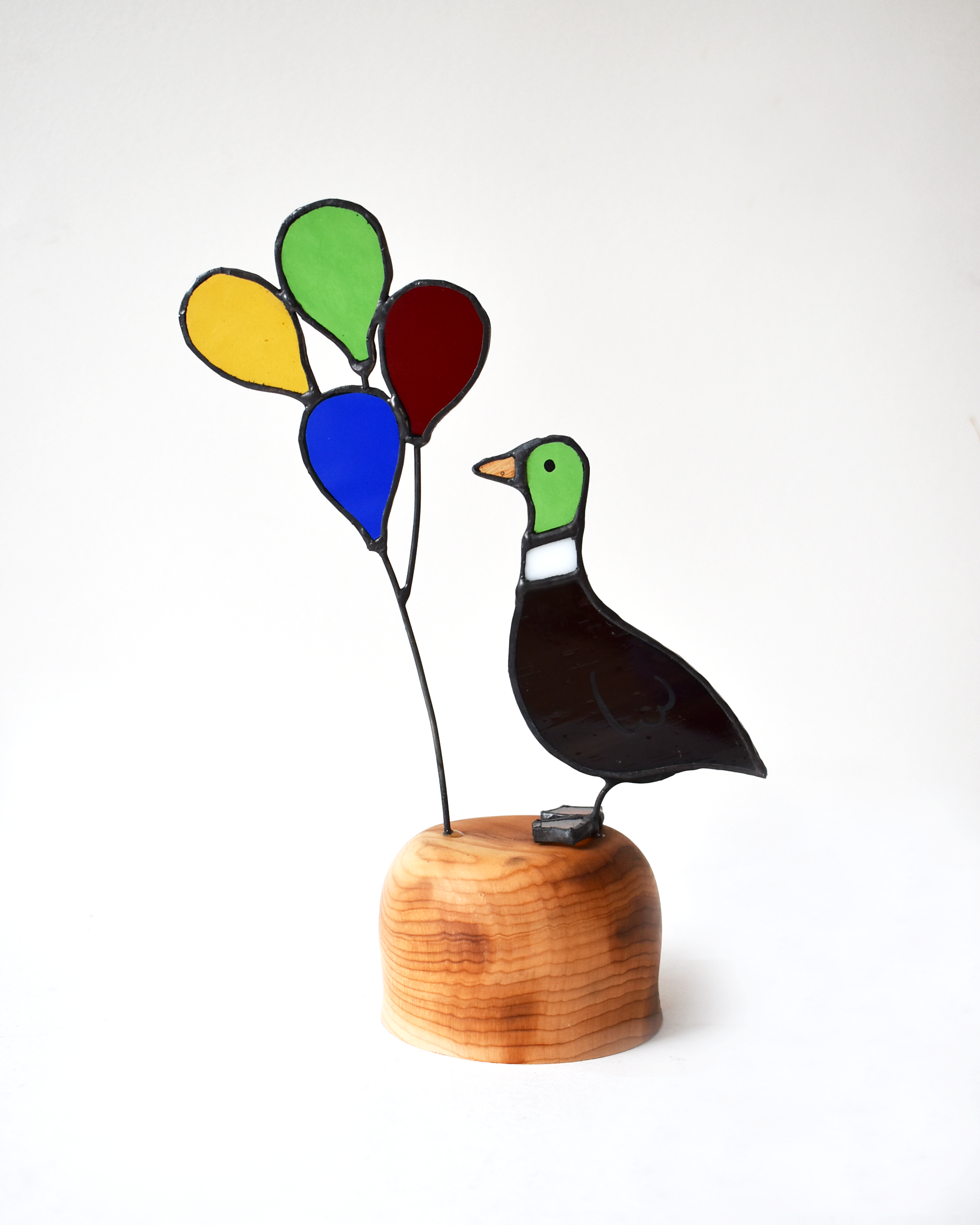Decorative glass bird with colorful balloons on a wooden base against a white background