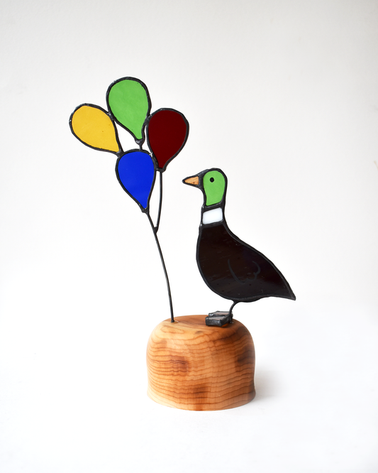 Decorative glass bird with colorful balloons on a wooden base against a white background